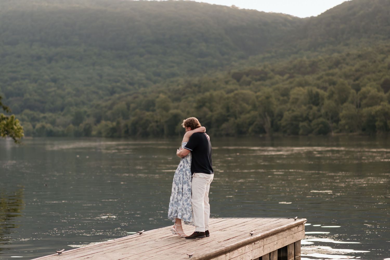 Couple hugs after surprise proposal near river and raccoon mountain