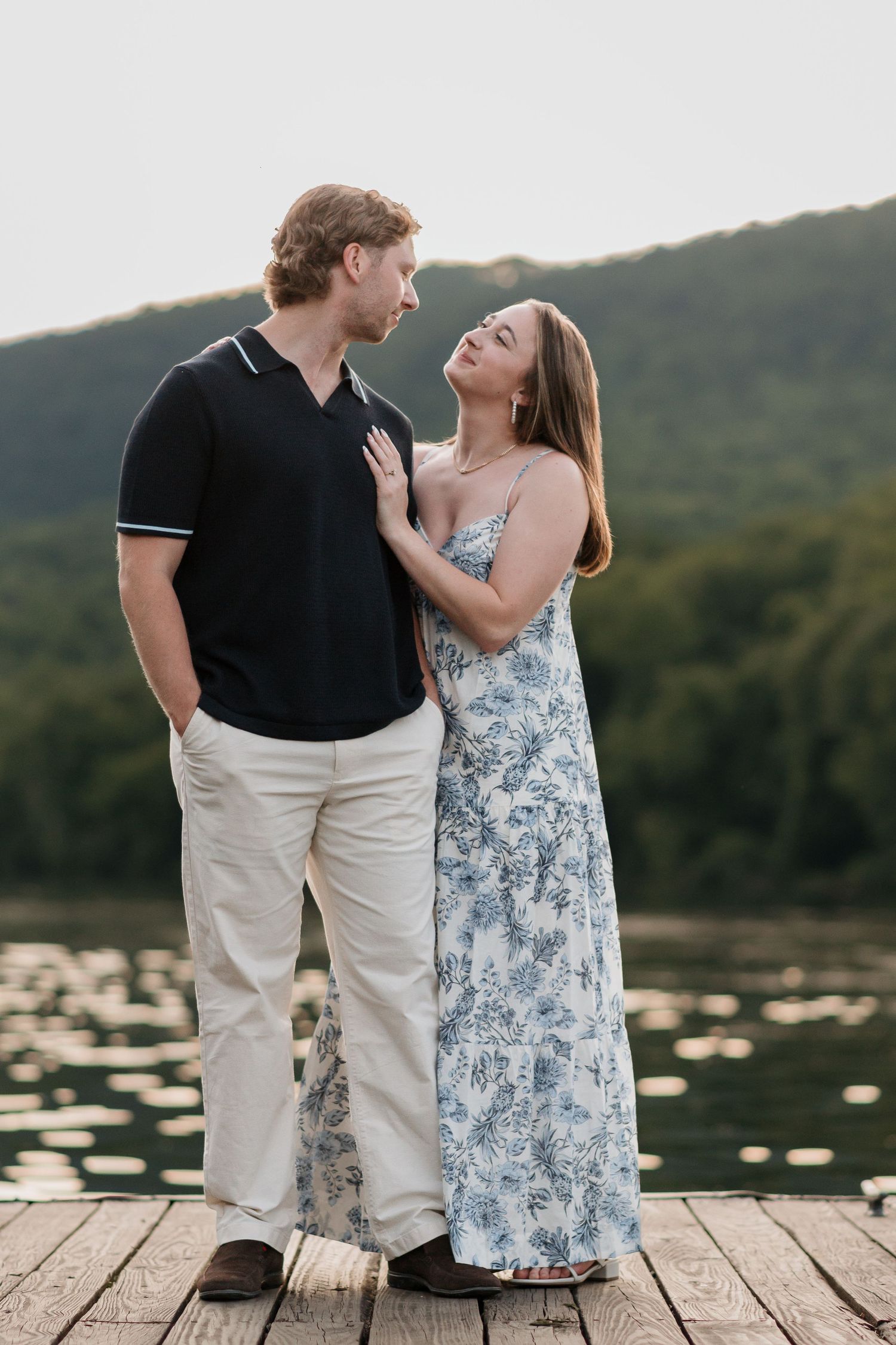 Couple standing close on dock near river and raccoon mountain during engagement session, looking at each other, golden hour