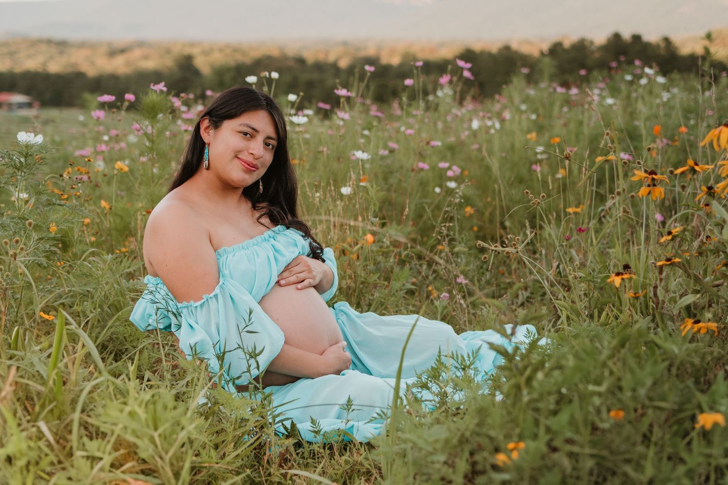 Itzayana sitting, looking at the camera in a wildflower field at Fox Mountain Farms, Chattanooga, TN – maternity session, soft summer light