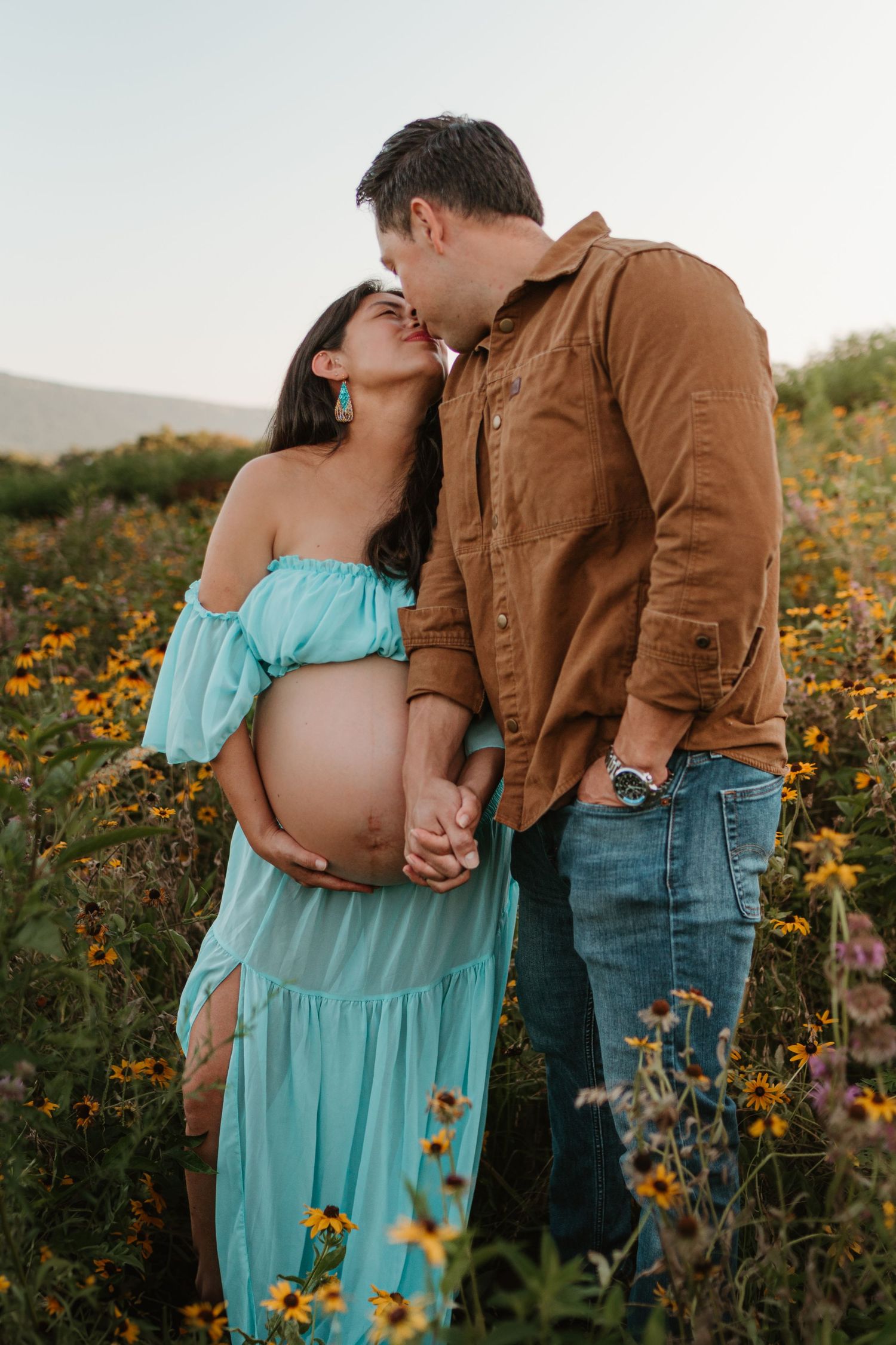 Couple kissing in a wildflower field at Fox Mountain Farms, Chattanooga, TN – maternity session, soft summer light