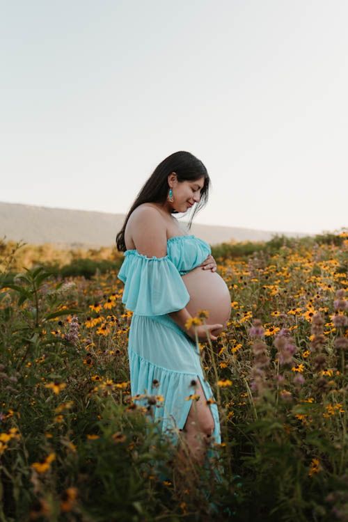 Expecting mom smiling down at baby bump standing in wildflower field during maternity golden hour session at Fox Mountain Farm, GA