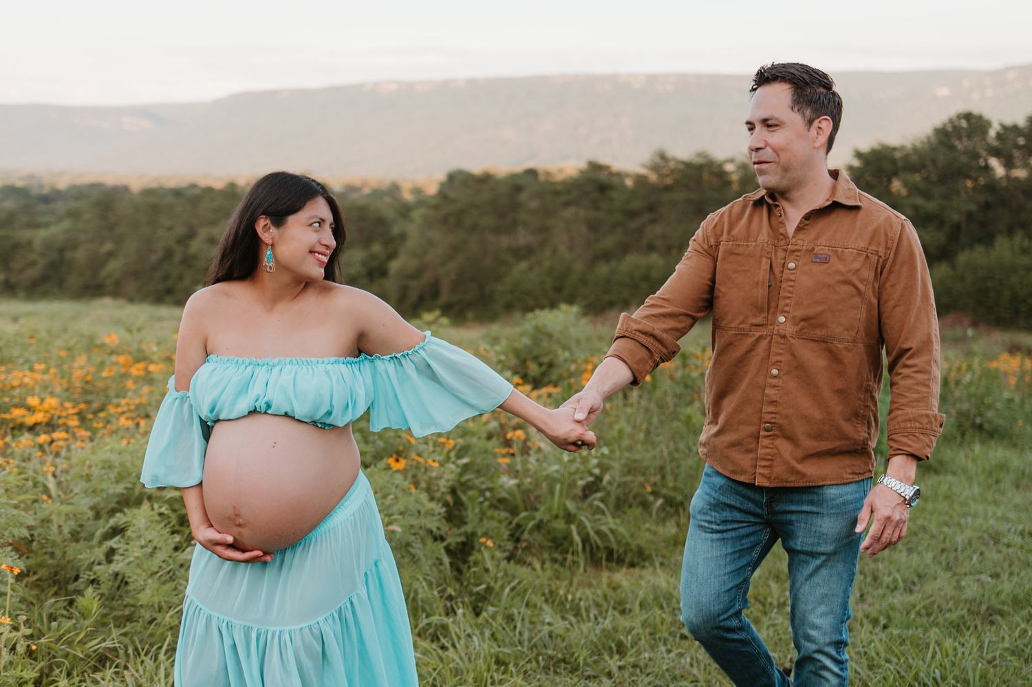Expecting couple walking and laughin in a wildflower field during golden hour maternity session at Fox Mountain Farm in Rising Fawn, Georgia