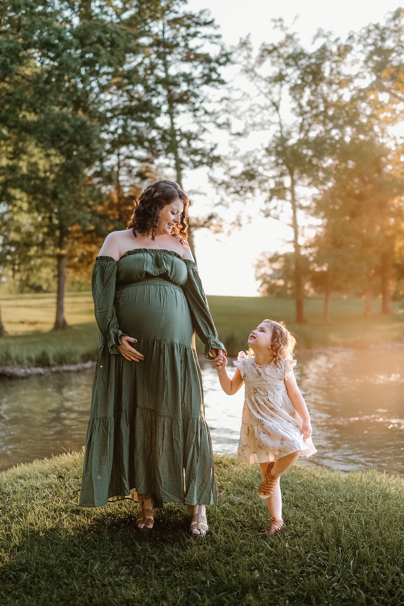 Mom and toddler holding hands looking at each other in Hixson, TN with bay behind them in warm, golden light