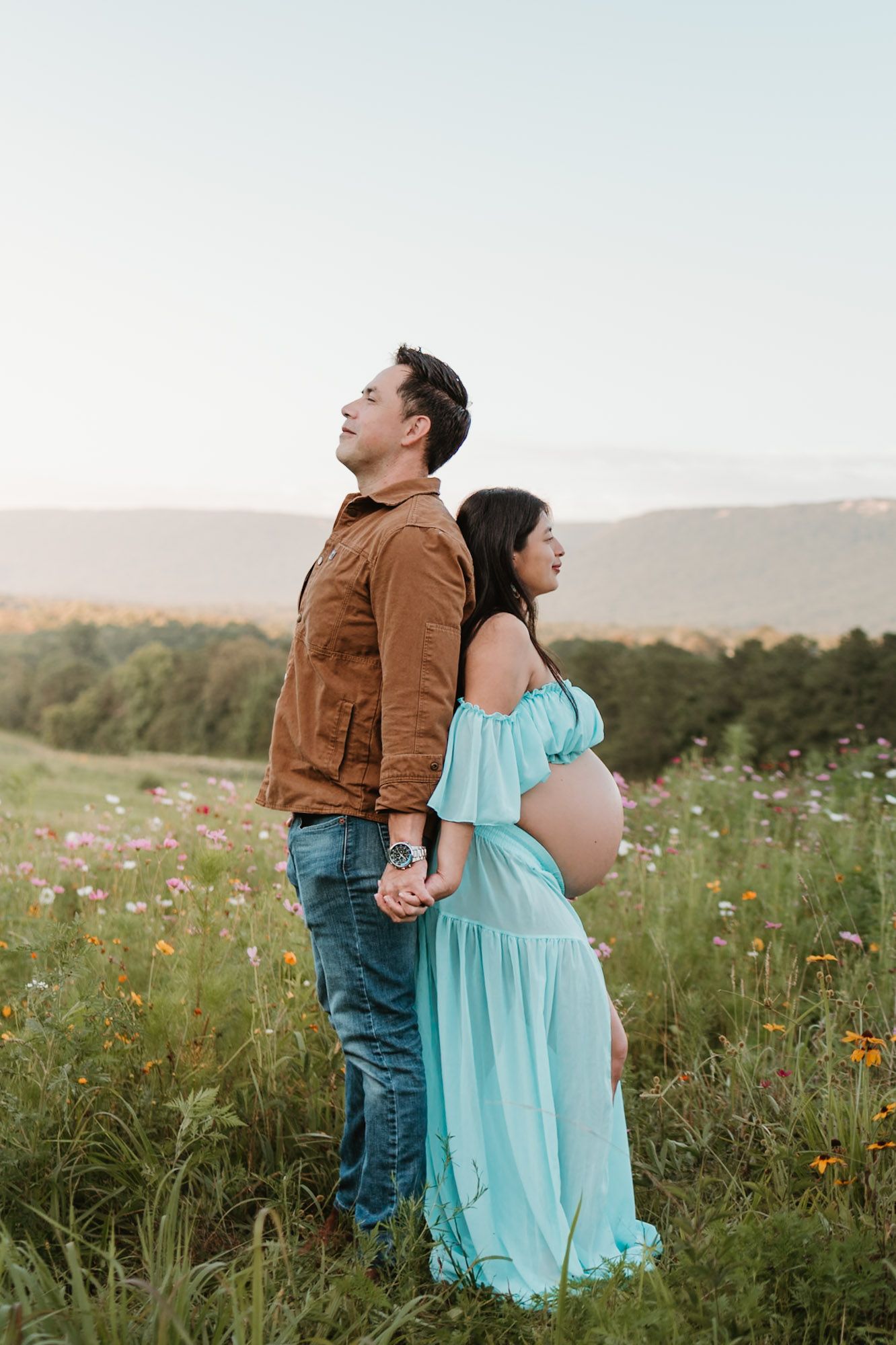 Expecting couple standing back to back in a wildflower field, golden hour maternity session at Fox Mountain Farm in Rising Fawn, Georgia
