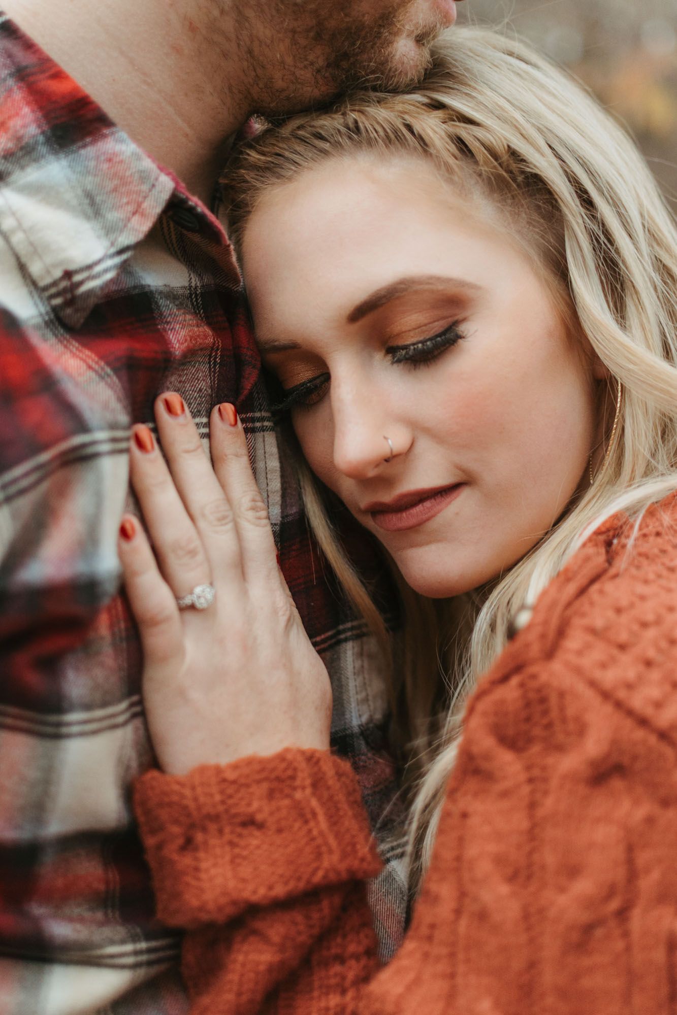 Intimate close up of couple, woman leaning her head on mans chest eyes closed, close up of ring during outdoor fall couples engagement