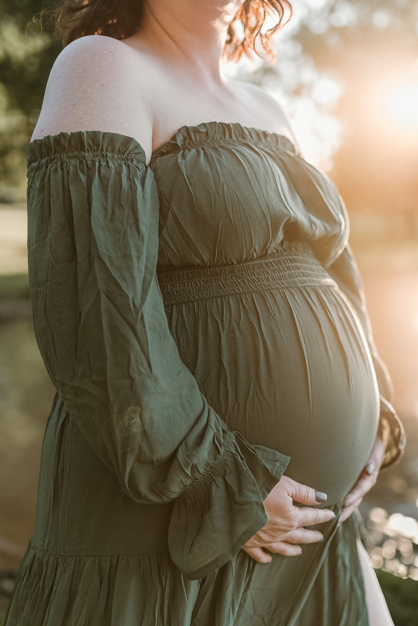 Close-up maternity photo of moms hands resting on baby bump, captured in soft natural light outdoors in Hixson, Tennessee.