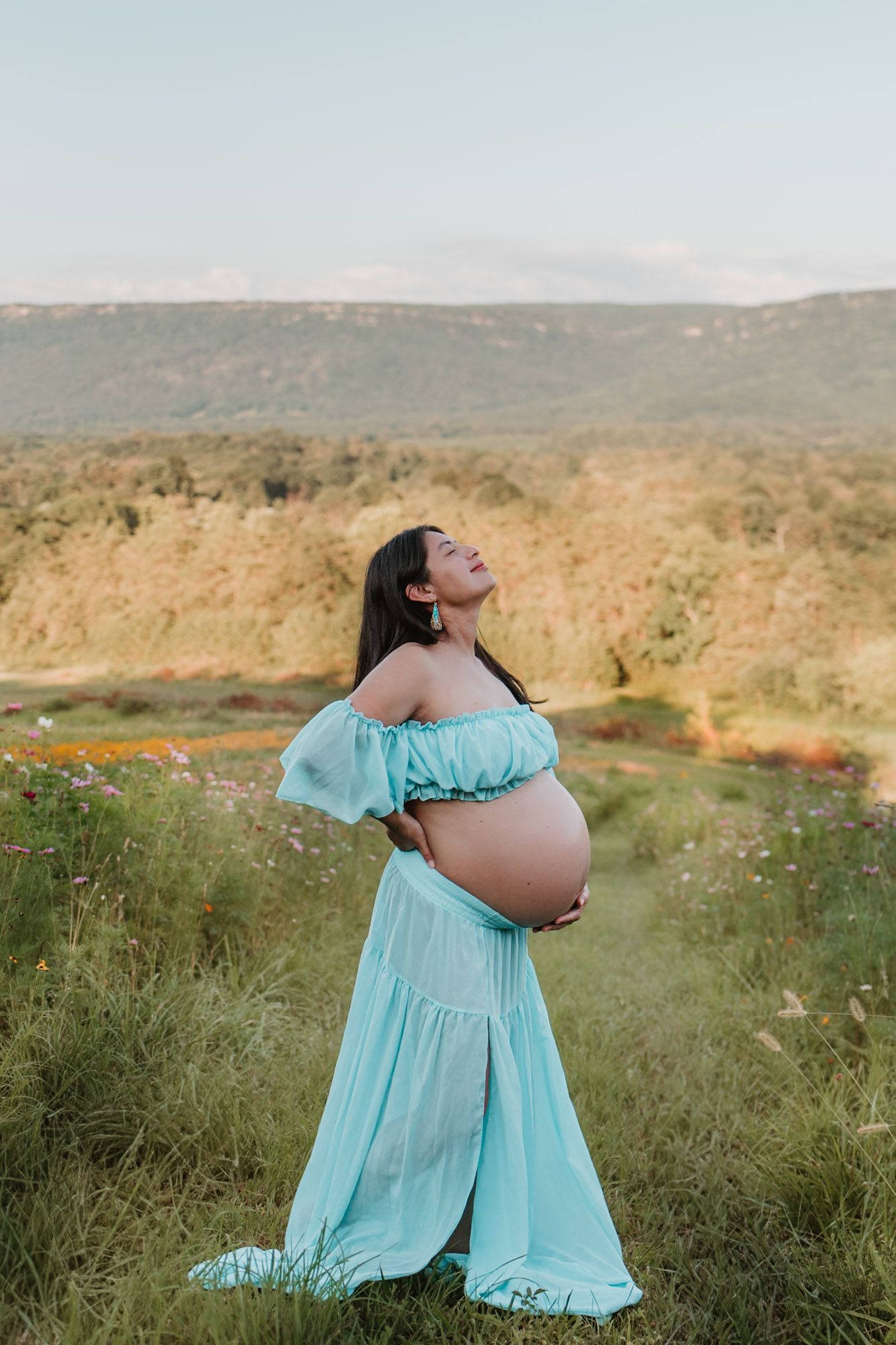 Expecting mom looking up in a wildflower field soaking in golden light during maternity session at Fox Mountain Farm in Rising Fawn, Georgia