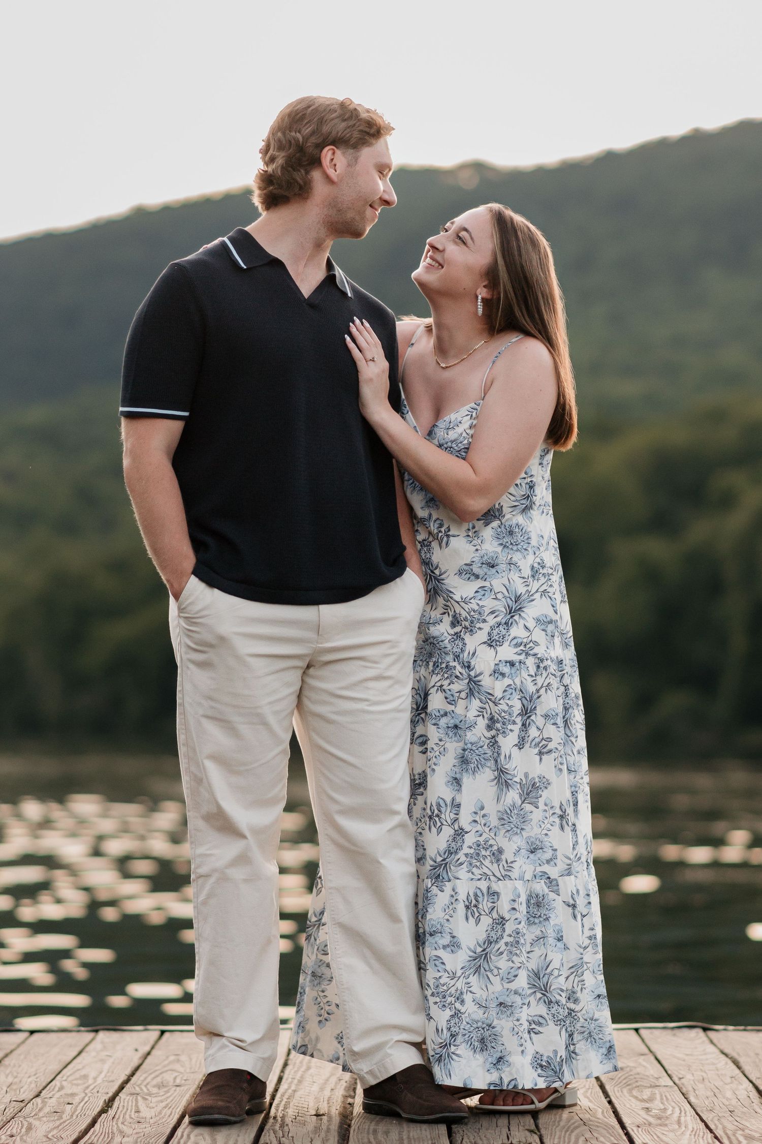 Couple standing close on dock near river and raccoon mountain during engagement session, golden hour