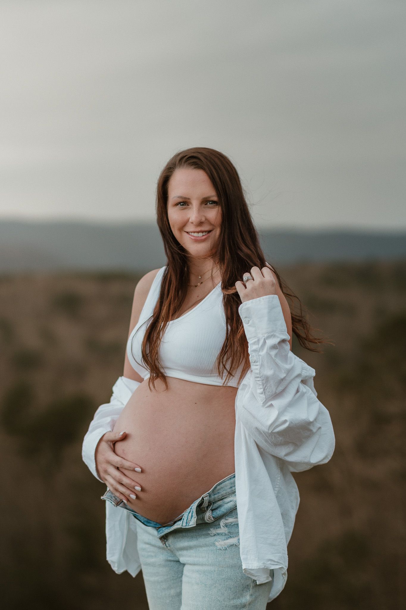 Expecting mom looking at camera holding her bump during maternity session on raccoon mountain in chattanooga tn, mountain overlook