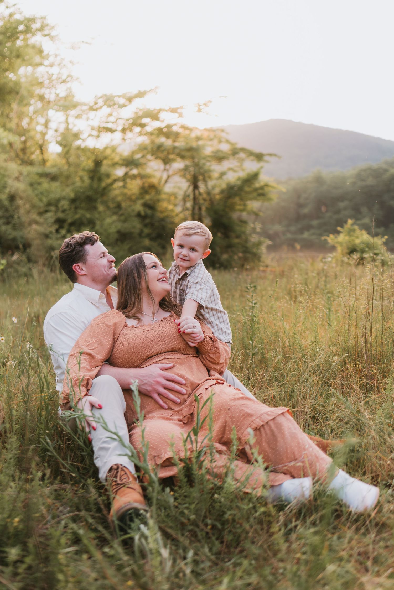 Family sitting in field looking at toddler in Chattanooga, TN – family maternity session, soft summer light, mountain background