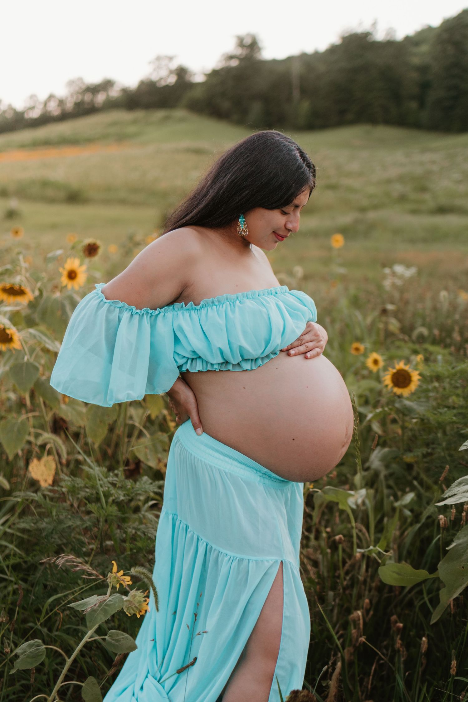 Itzayana looking down at belly in a sunflower field at Fox Mountain Farms, Chattanooga, TN – maternity session, soft summer light