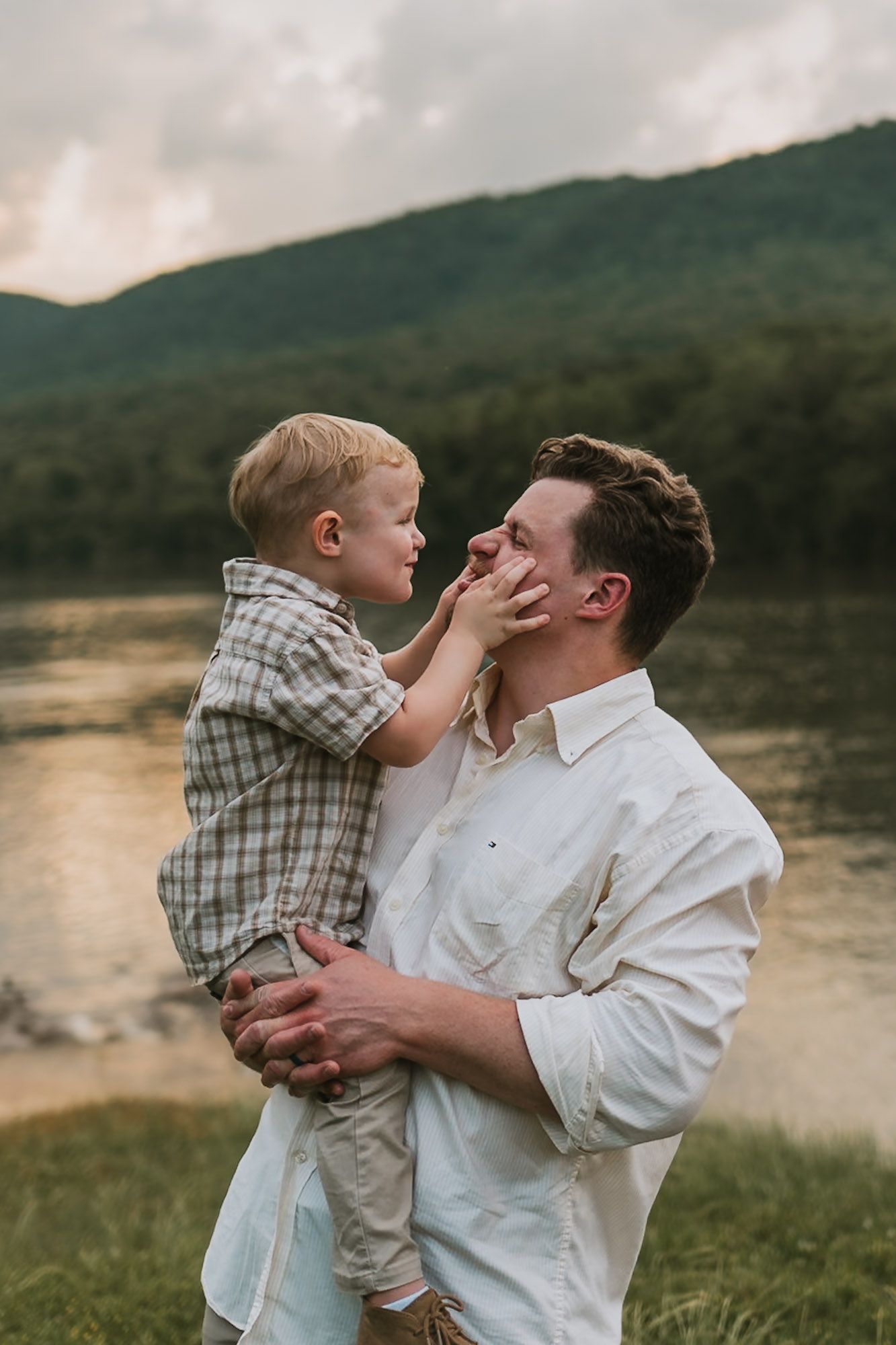 Dad holding toddler in field with water and mountains in background during family session at raccoon mountain, Chattanooga TN