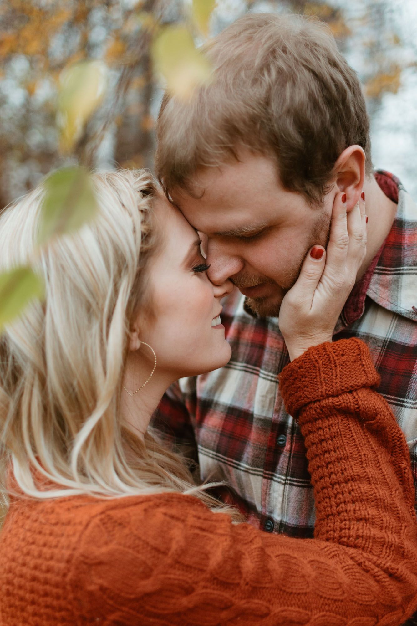 Intimate close up of couple almost kissing, her hand on his cheek during outdoor fall couples engagement session