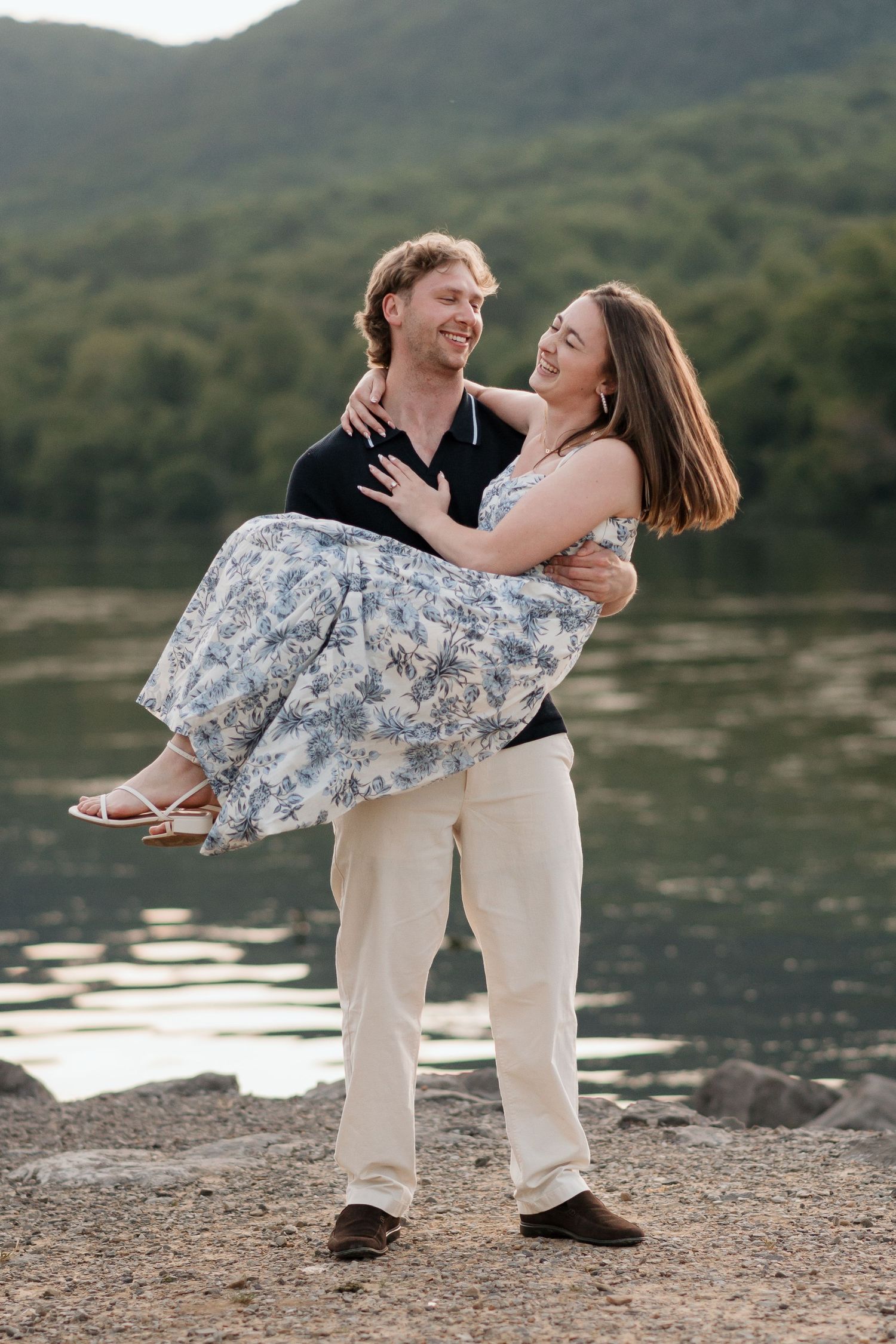 Man holding girlfriend while spinning her around during surprise proposal session near river and raccoon mountain