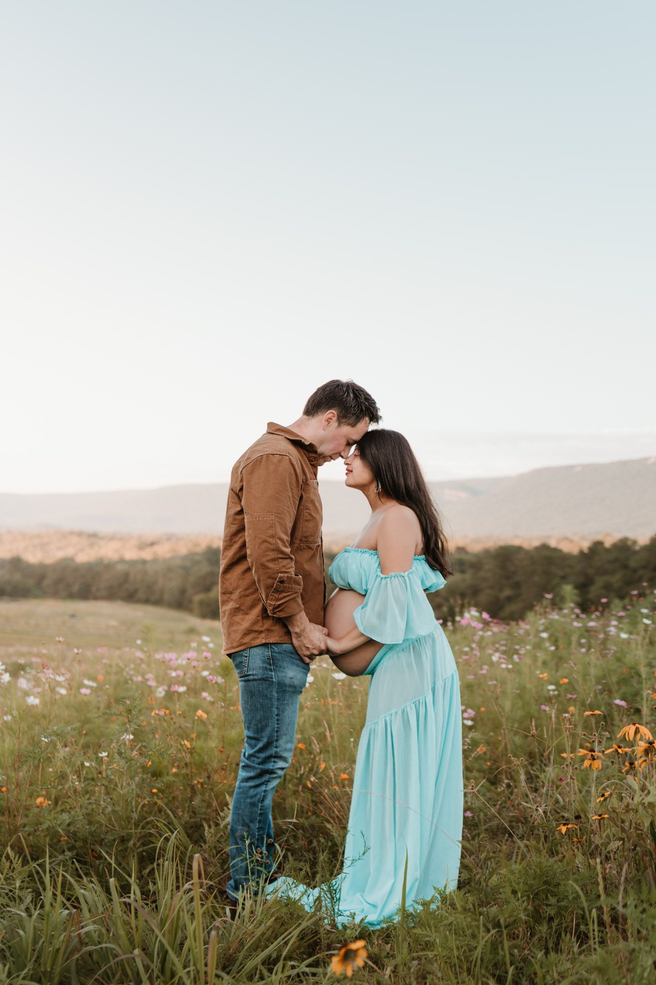Expecting couple forehead to forehead in wildflower field during golden hour maternity session at Fox Mountain Farm in Rising Fawn, Georgia
