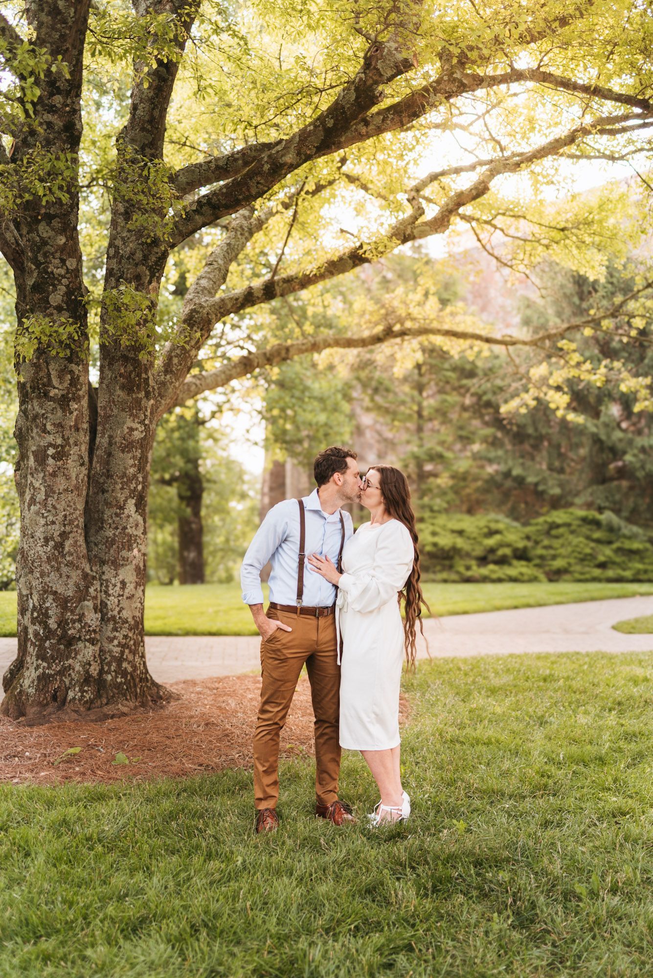 Couple standing and kissing in field with morning light through trees during outdoor morning session on lookout mountain Georgia