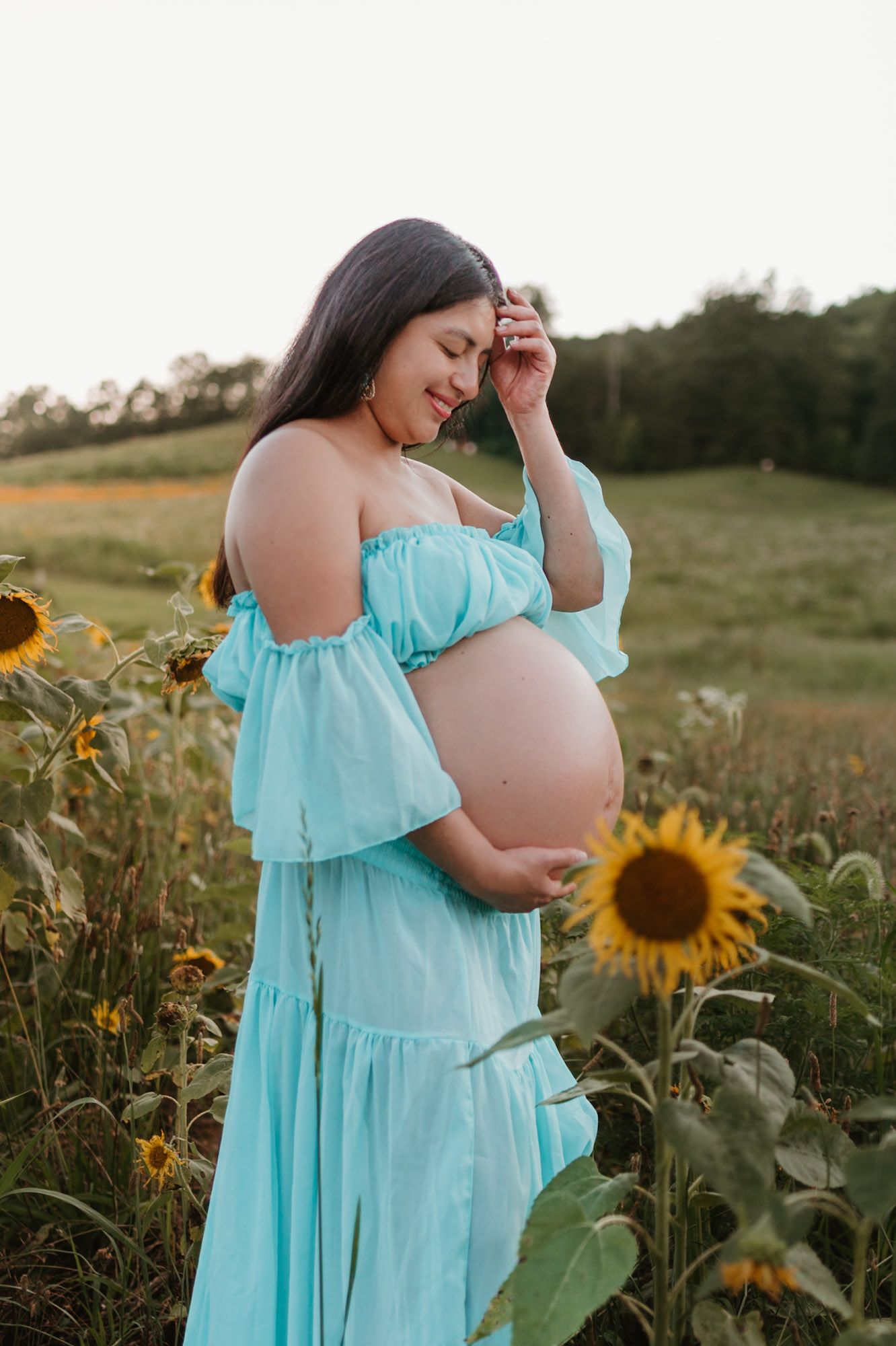 Expecting mom standing in a sunflower field playing with hair during maternity session at Fox Mountain Farm in Rising Fawn, Georgia