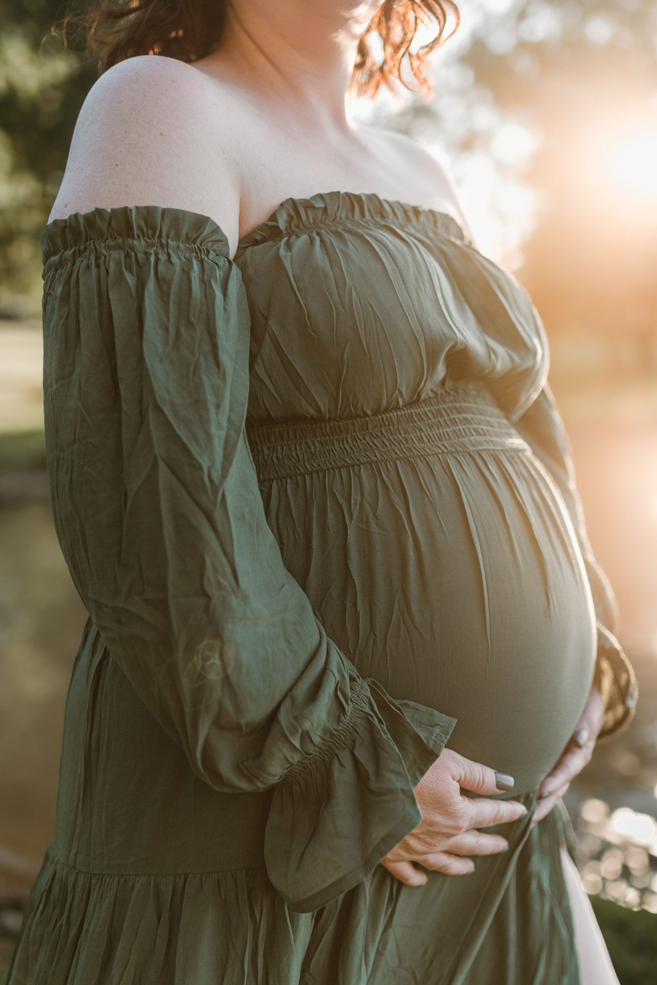Close up of expectant moms bump in  flowy green dress near water at family maternity golden hour session at Chester Frost park in Hixson, TN