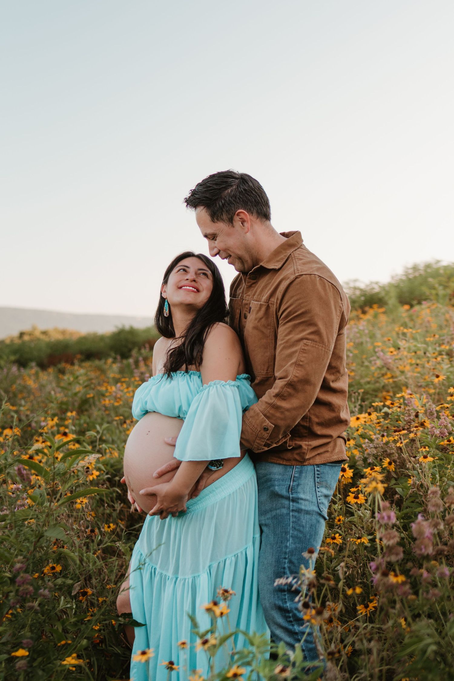 Couple looking at eachother in a wildflower field at Fox Mountain Farms, Chattanooga, TN – maternity session, soft summer light