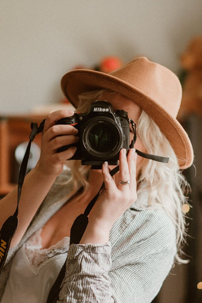 Chattanooga lifestyle photographer taking a photo with a Nikon camera indoors, wearing a neutral outfit and wide brim hat