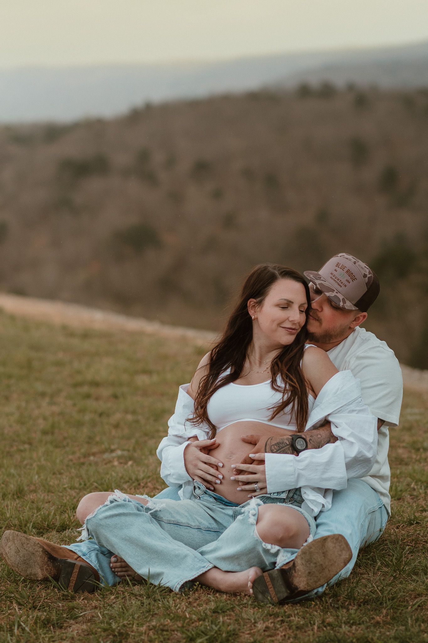 Expecting couple sitting, him kissing her cheek, holding her belly during maternity session on raccoon mountain in chattanooga tn, overlook