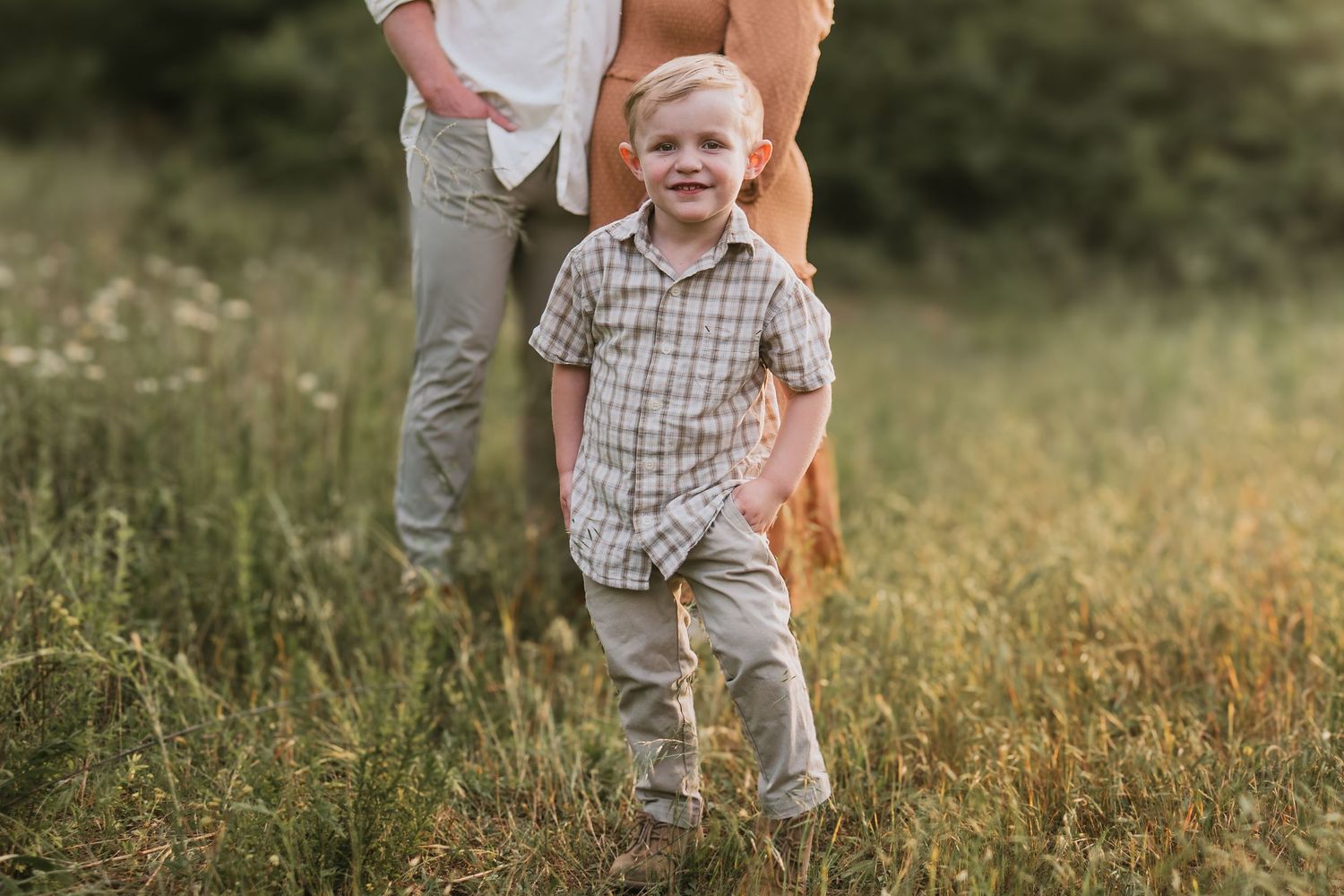 Toddler looking at camera with parents in background in a field in Chattanooga, TN – family maternity session, soft summer light