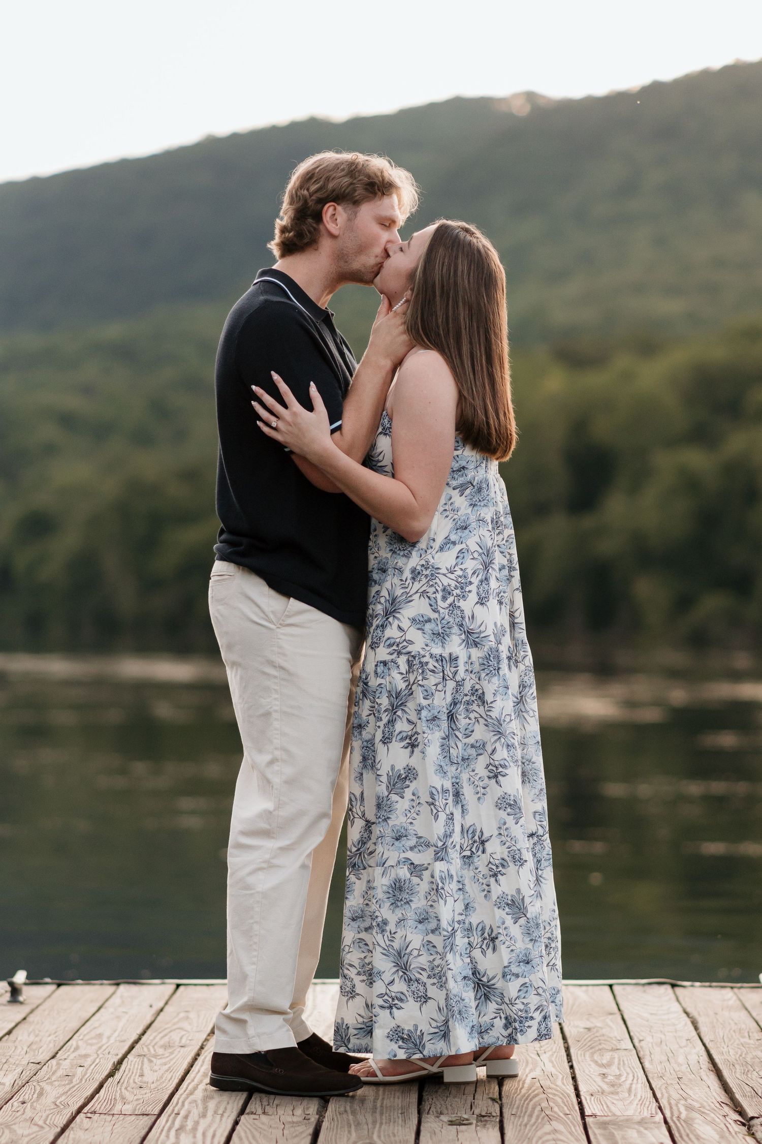 Couple kissing on dock near river and raccoon mountain after surprise proposal, summer evening golden hour