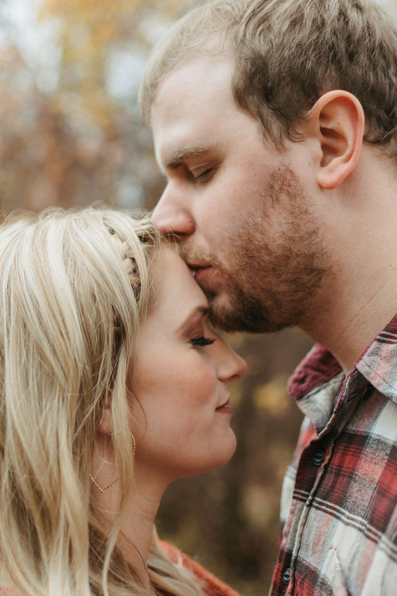 Close up of couple, man kissing woman's forehead during outdoor fall couples engagement session, intimate moment