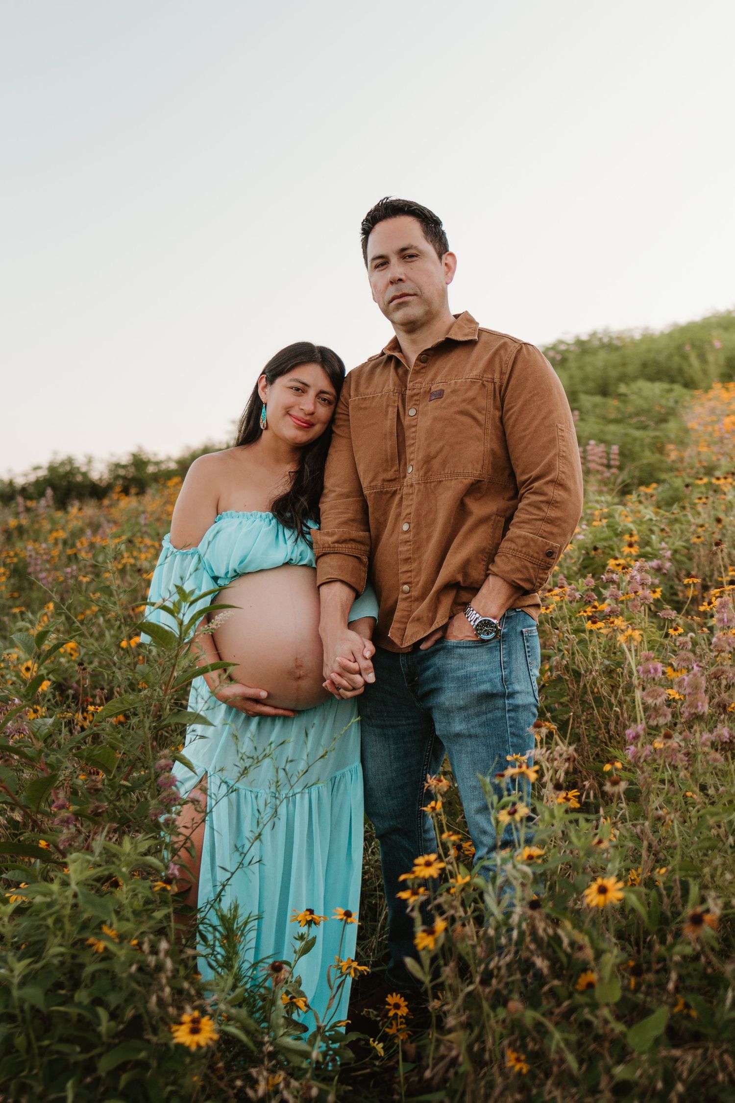 Couple looking at camera in a wildflower field at Fox Mountain Farms, Chattanooga, TN – maternity session, soft summer light