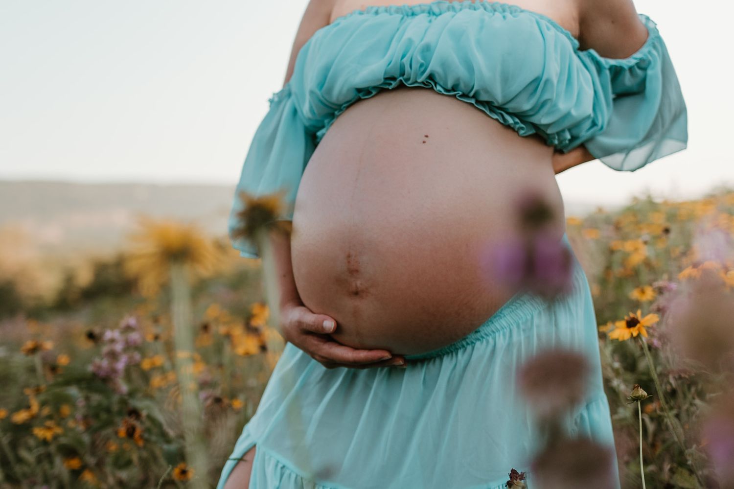 Close up of expectant moms bump in a wildflower field during golden hour maternity session at Fox Mountain Farm in Rising Fawn, Georgia