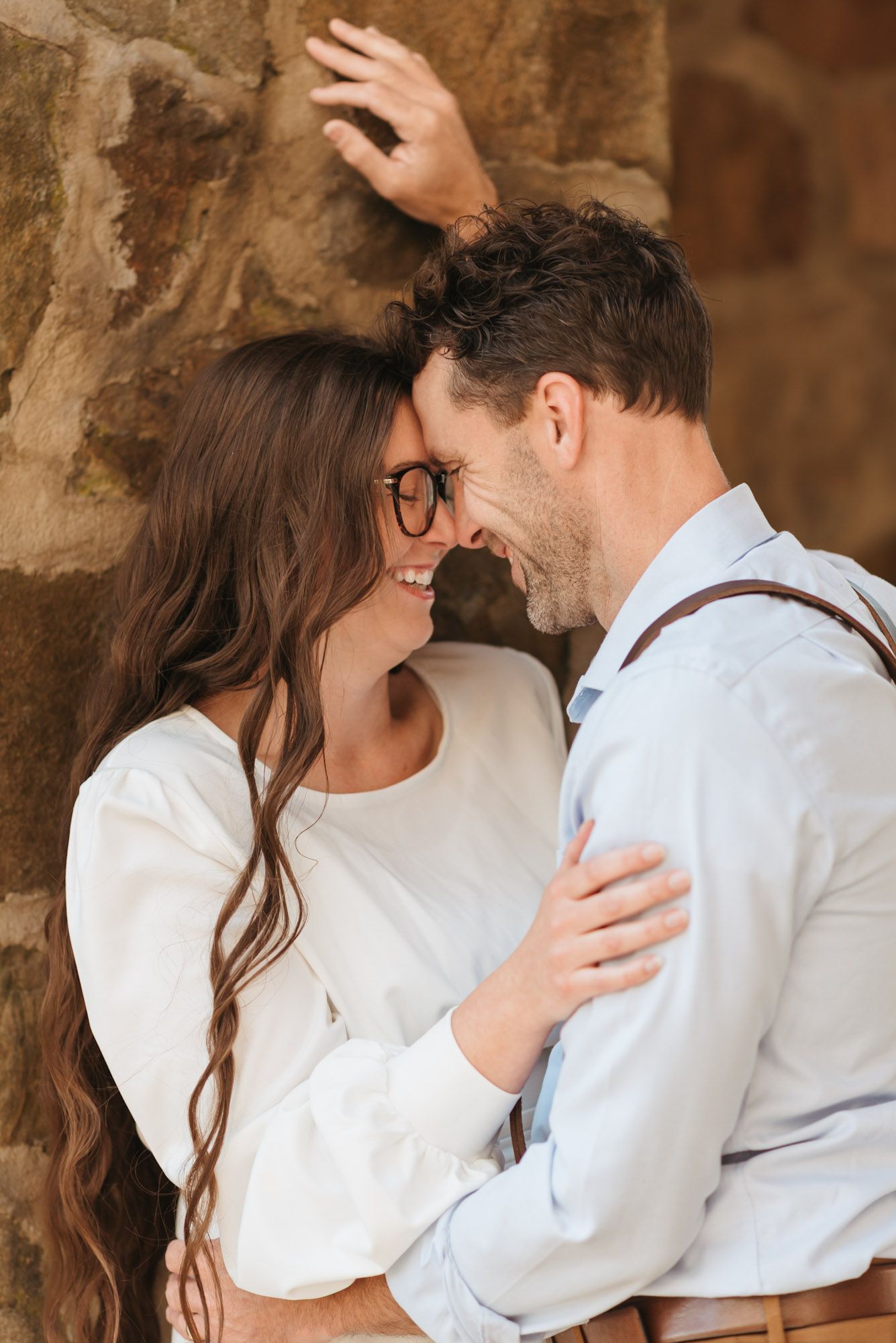 Couple against stone wall forehead to forehead laughing, his hand above her during outdoor morning session on lookout mountain Georgia