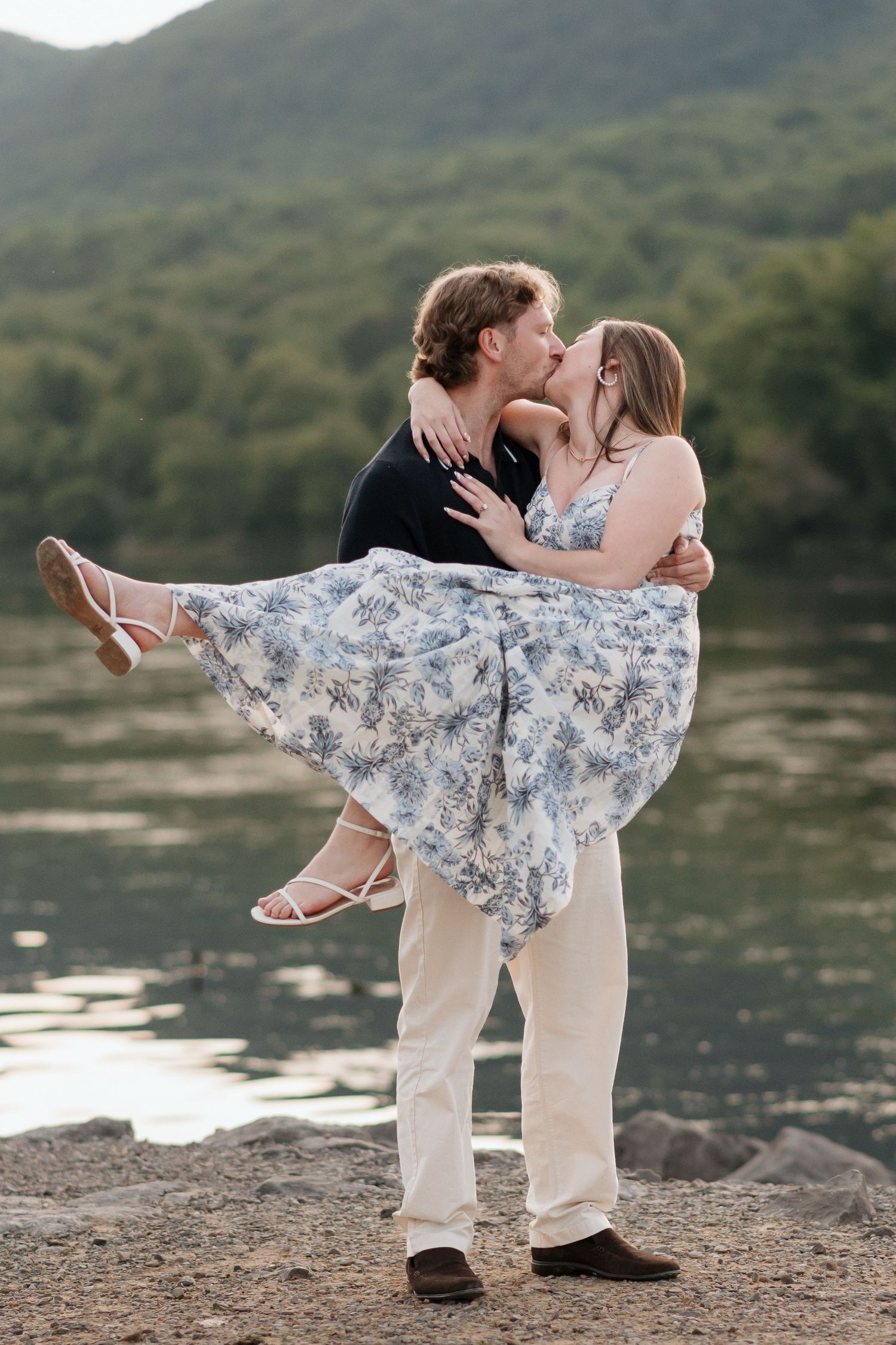 Man holding and kissing girlfriend while spinning her around during surprise proposal session near river and raccoon mountain