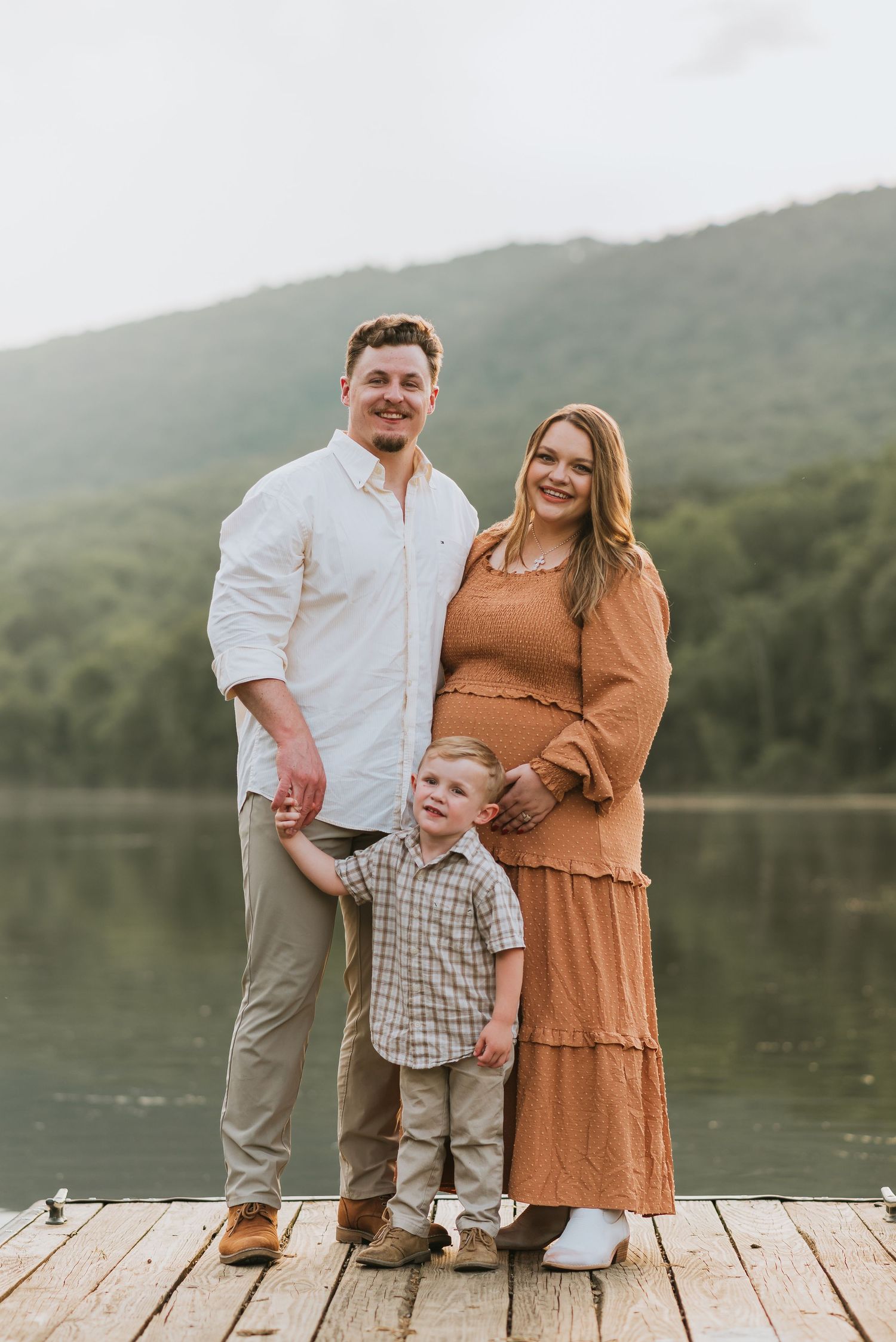 Family looking at camera on a dock in Chattanooga, TN – family maternity session, soft summer light, mountains and water