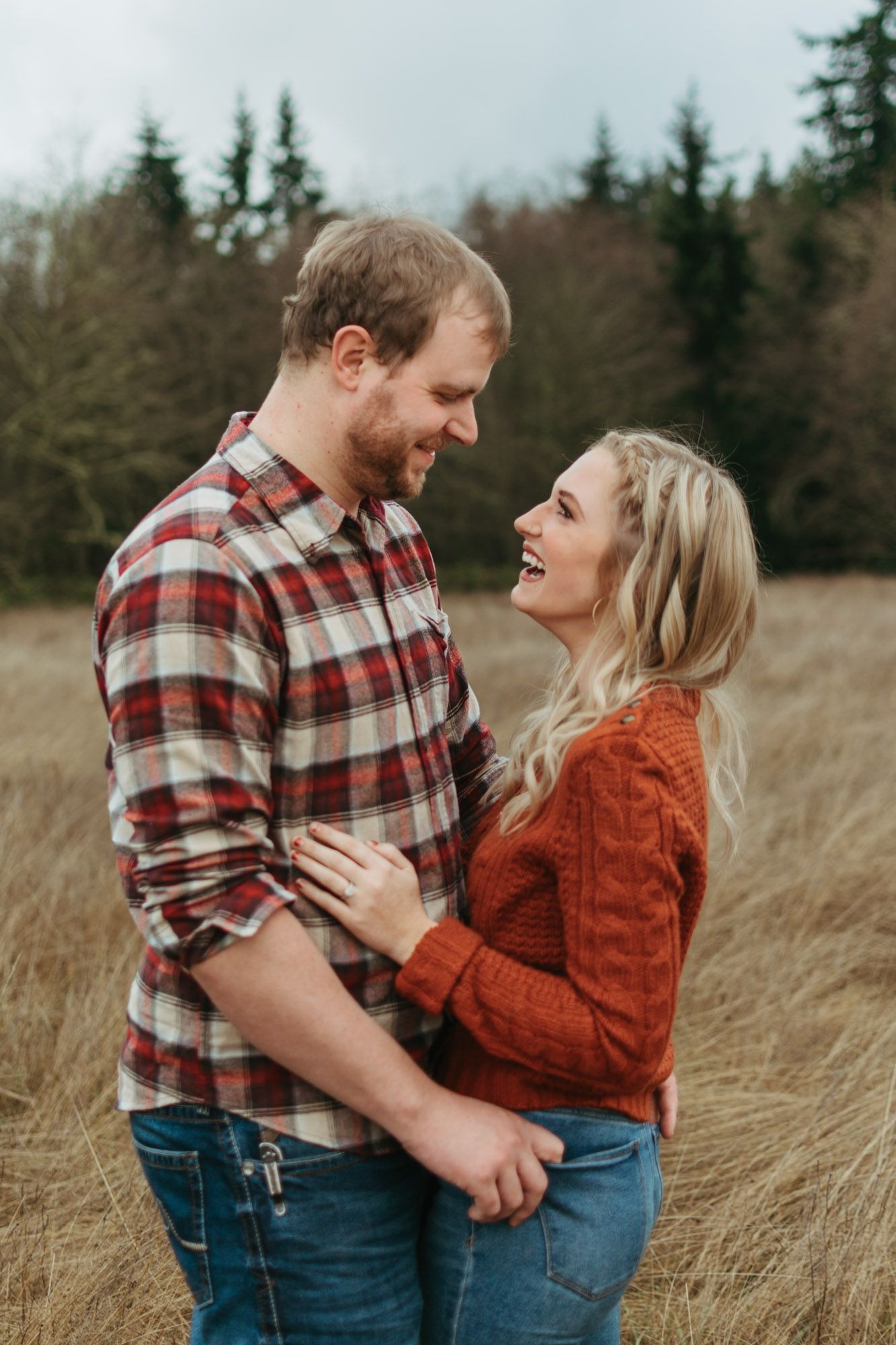 Couple standing belly buttons together looking at each other laughing during outdoor fall couples engagement session