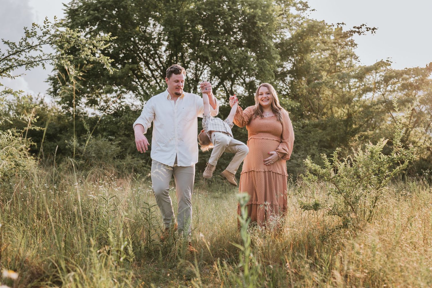 Expecting couple walking in field lifting toddler up, maternity session at raccoon mountain chattanooga TN