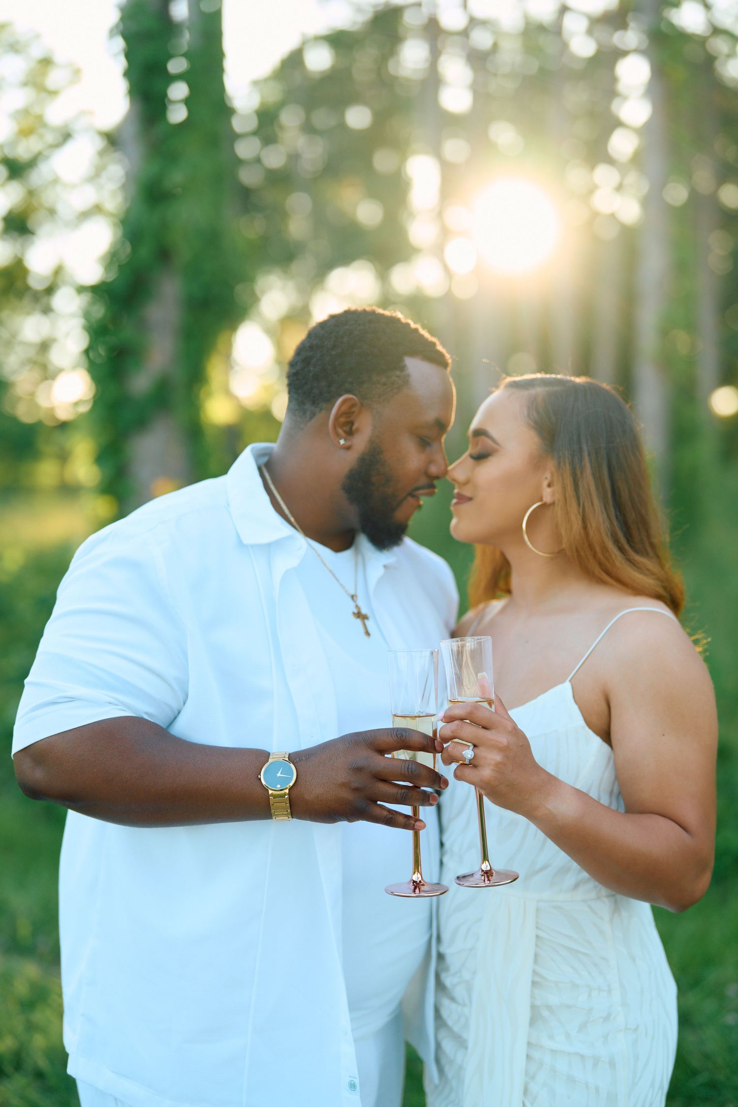 Couple sharing intimate moment with wine glasses in sunlit forest setting.