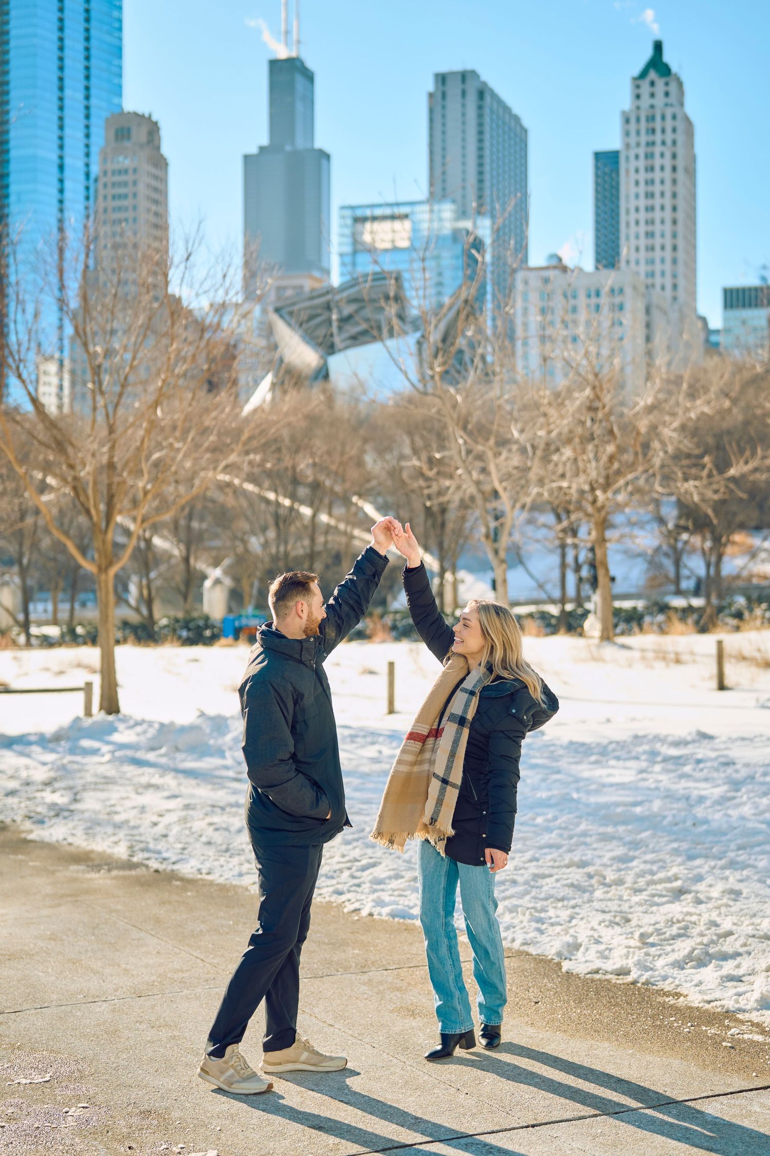 A couple high-fives against Chicago's iconic skyline on a snowy winter day in a city park.
