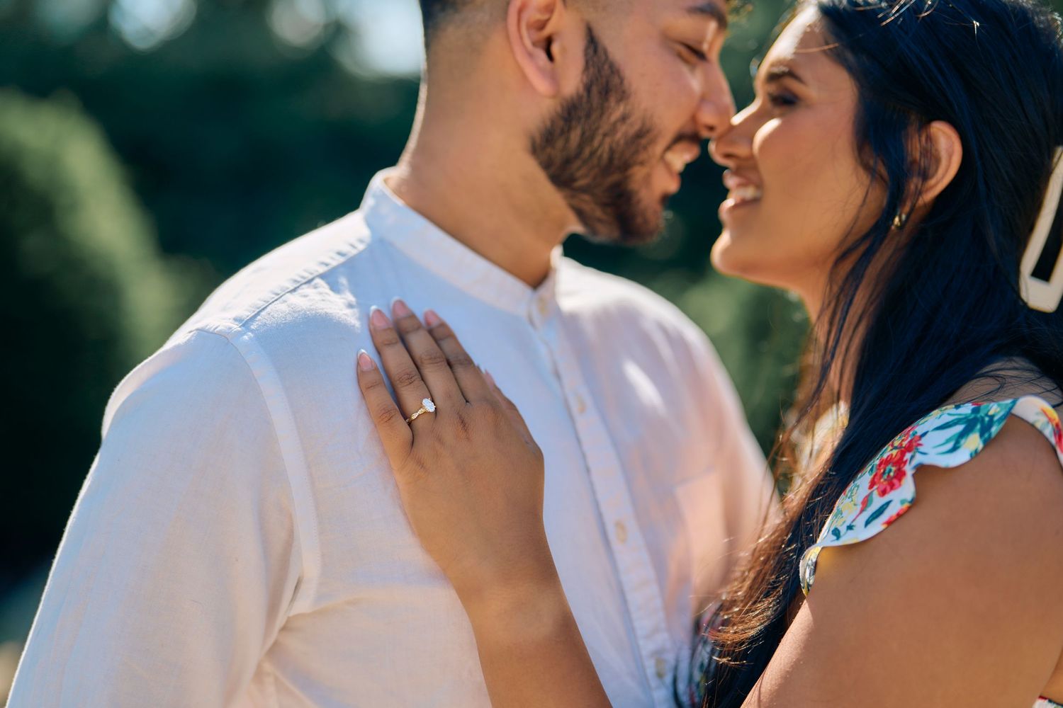 A couple shares a tender romantic moment outdoors on a sunny day.