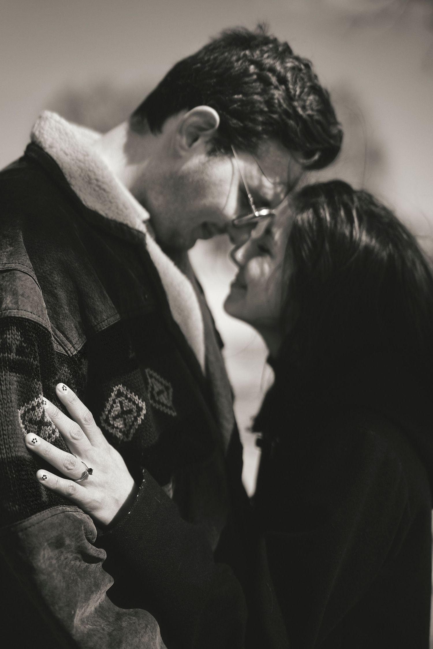 A romantic black and white photograph showing an intimate moment between a couple in winter clothing about to kiss.