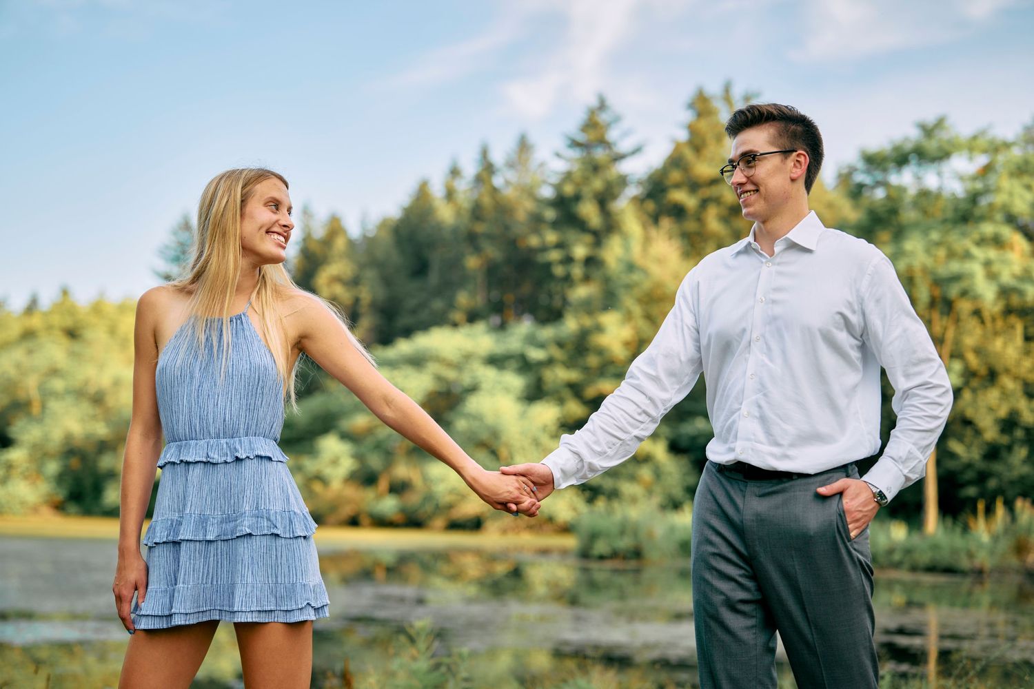 A couple holds hands while enjoying a sunny afternoon in a scenic forest setting with evergreen trees in background.