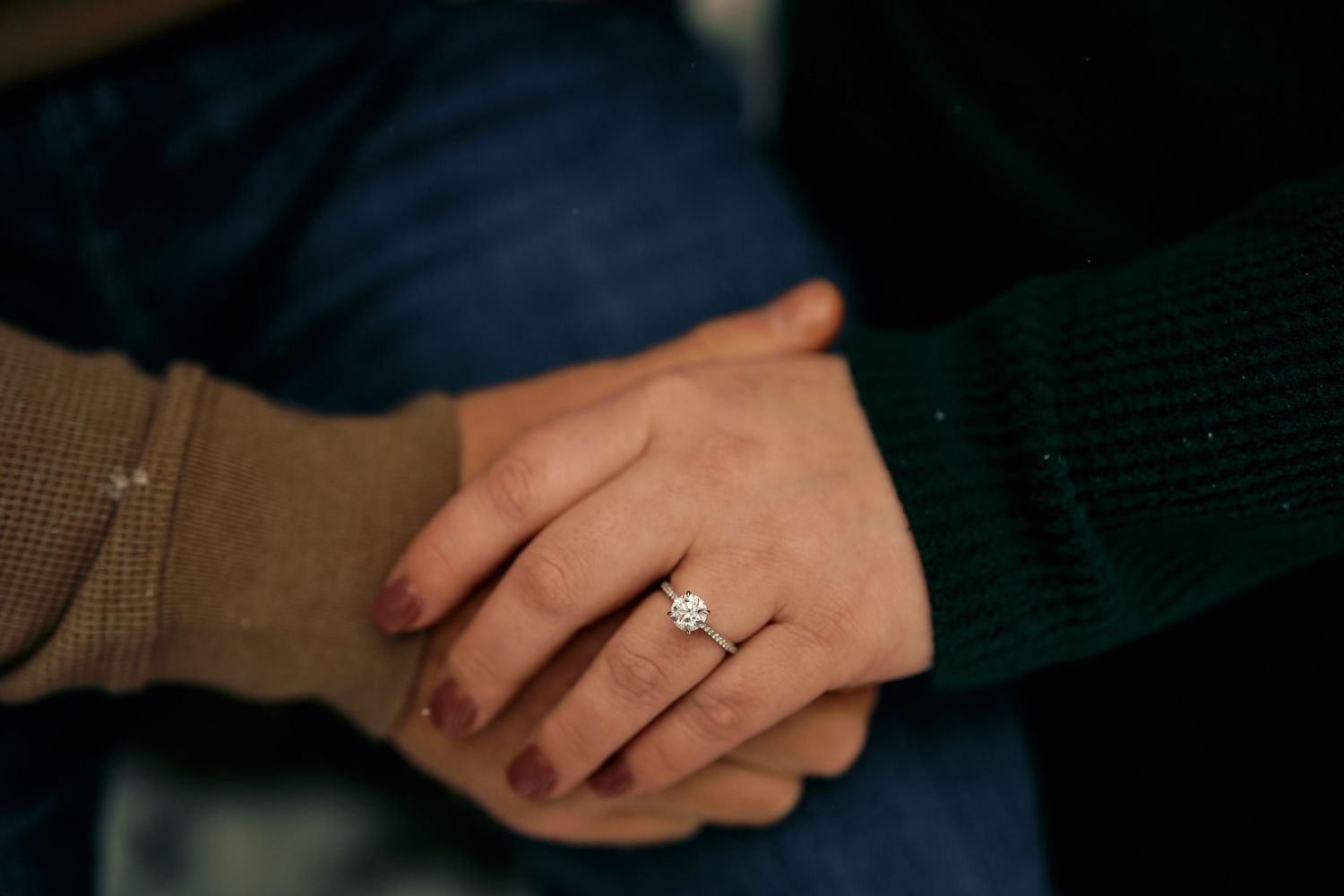 Close-up shot of clasped hands showing an engagement ring on a finger.
