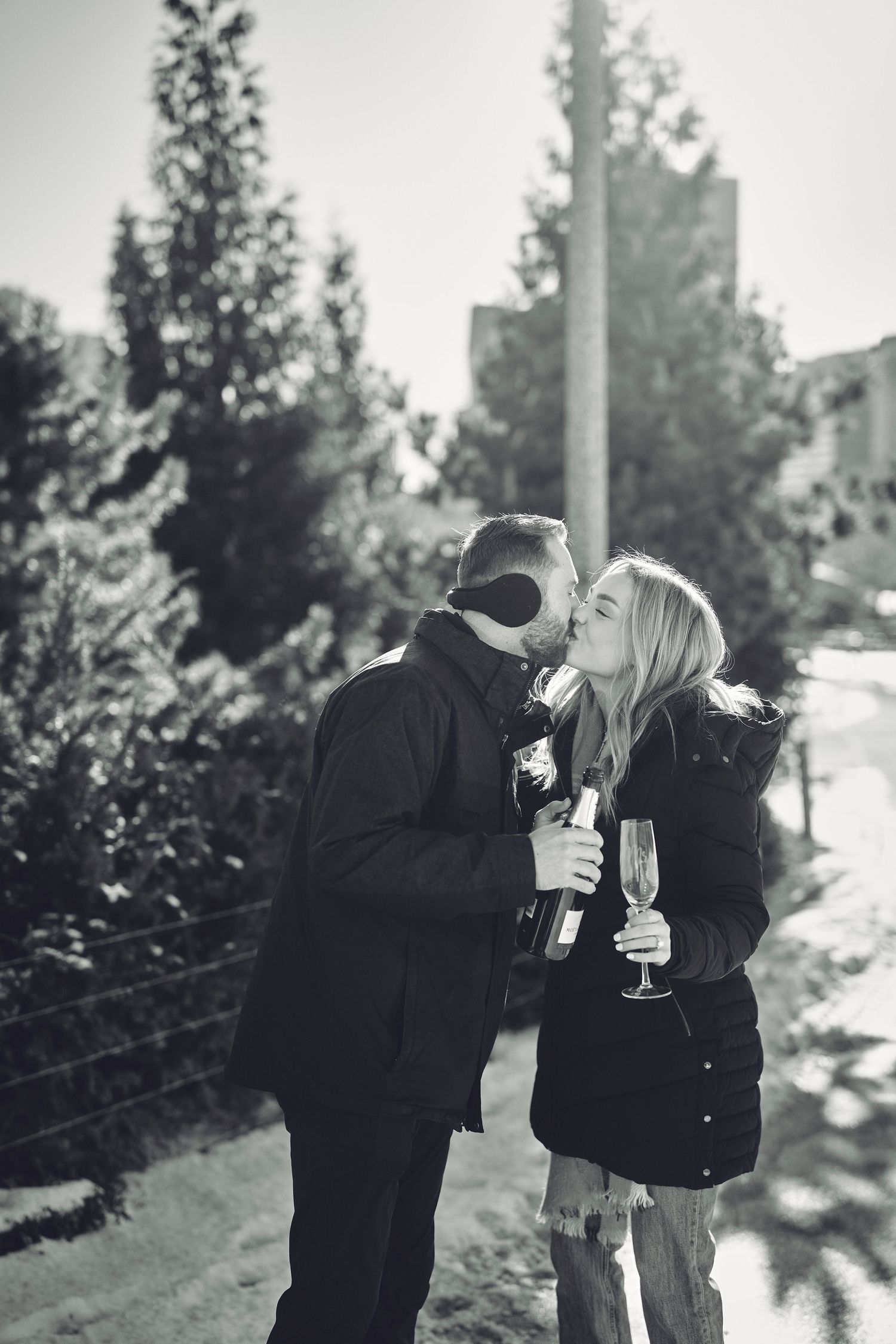 A couple sharing a romantic winter moment while holding champagne glasses in a snowy outdoor setting.