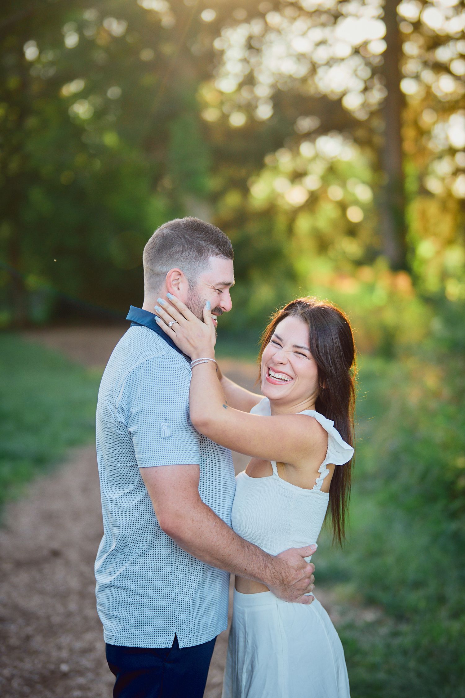 A couple shares a tender romantic moment on a sunlit forest path during a warm summer evening.