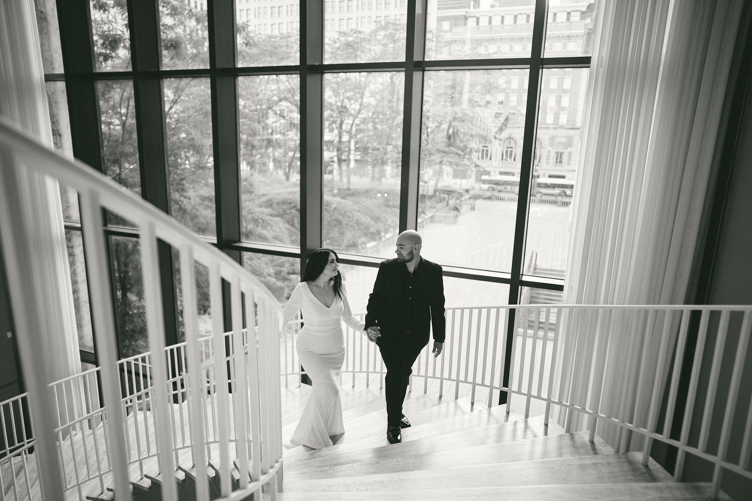 Two figures walk down elegant white spiral staircase in black and white photograph.