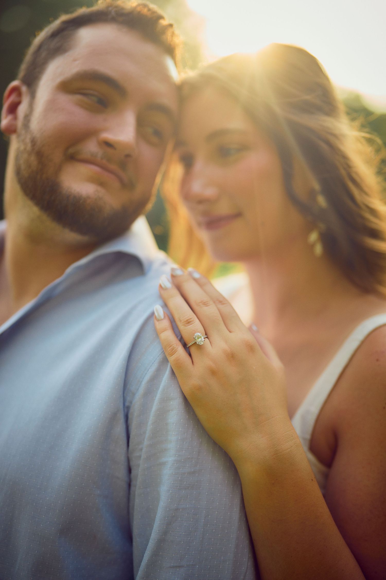 A romantic engagement photo shows a couple embracing in golden sunlight with a sparkling diamond ring on display.
