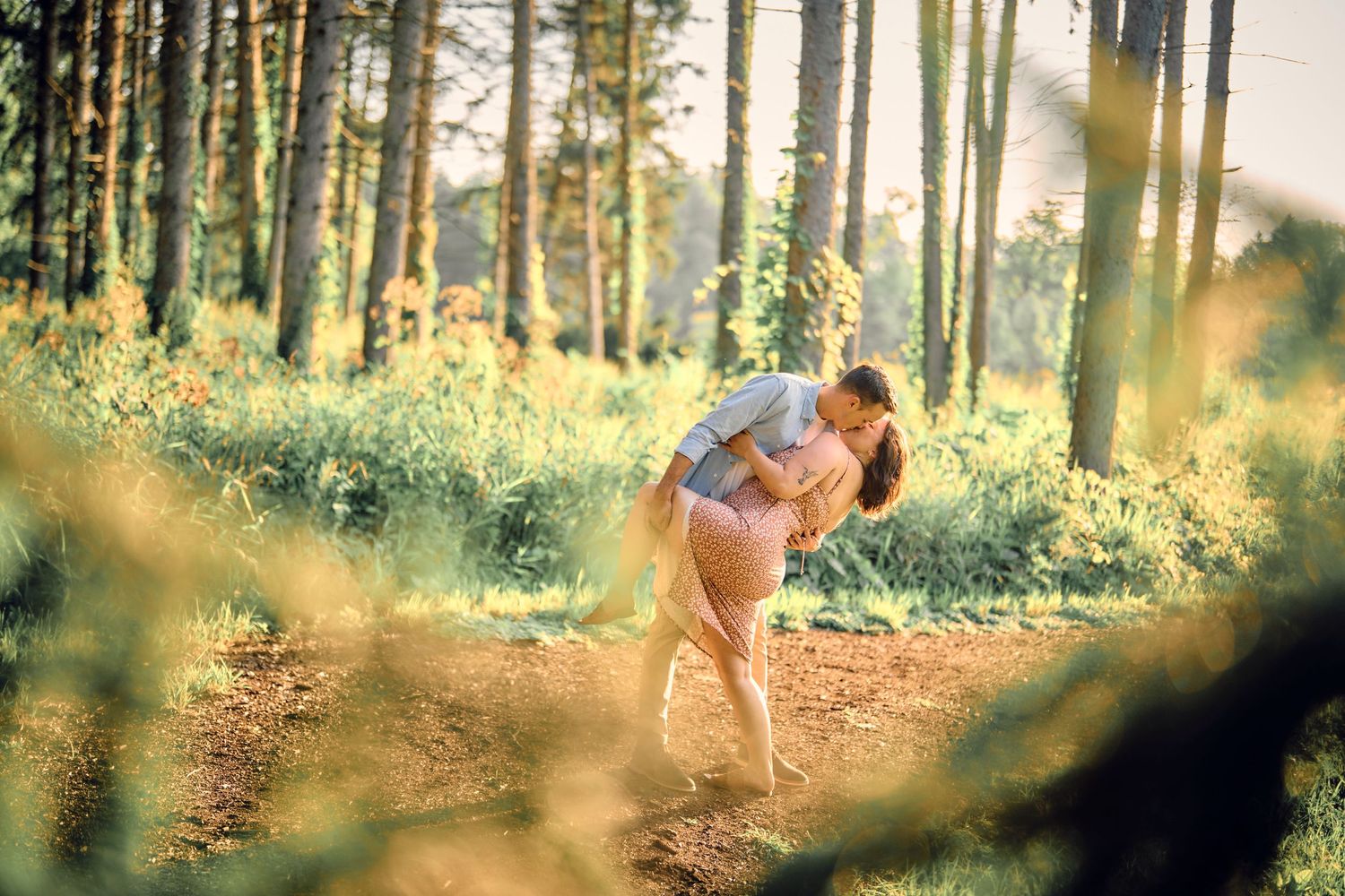 Dancing couple captured in romantic sunlit forest setting with dreamy golden light filtering through trees.