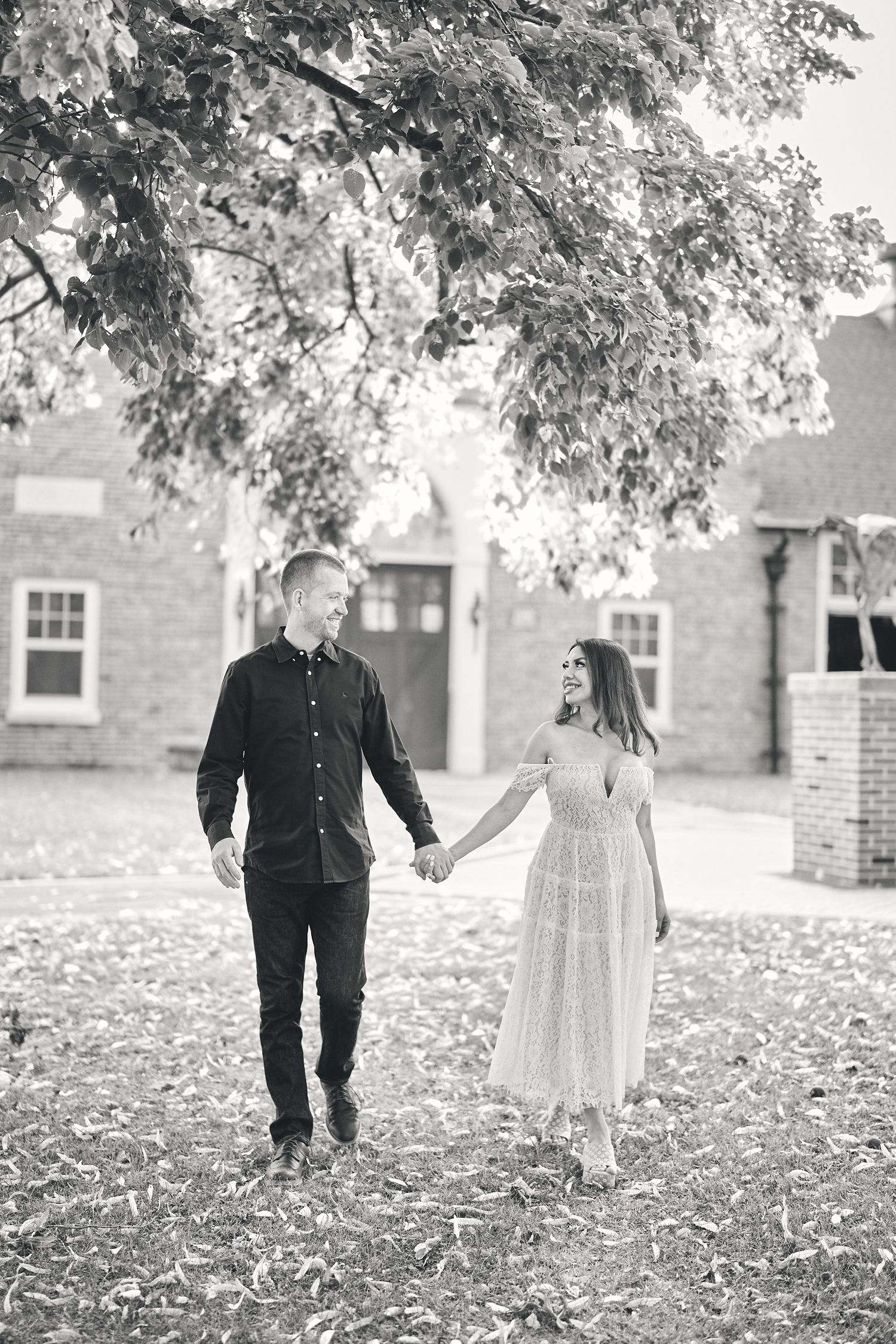 Couple walking together holding hands on autumn day among fallen leaves in black and white photo.