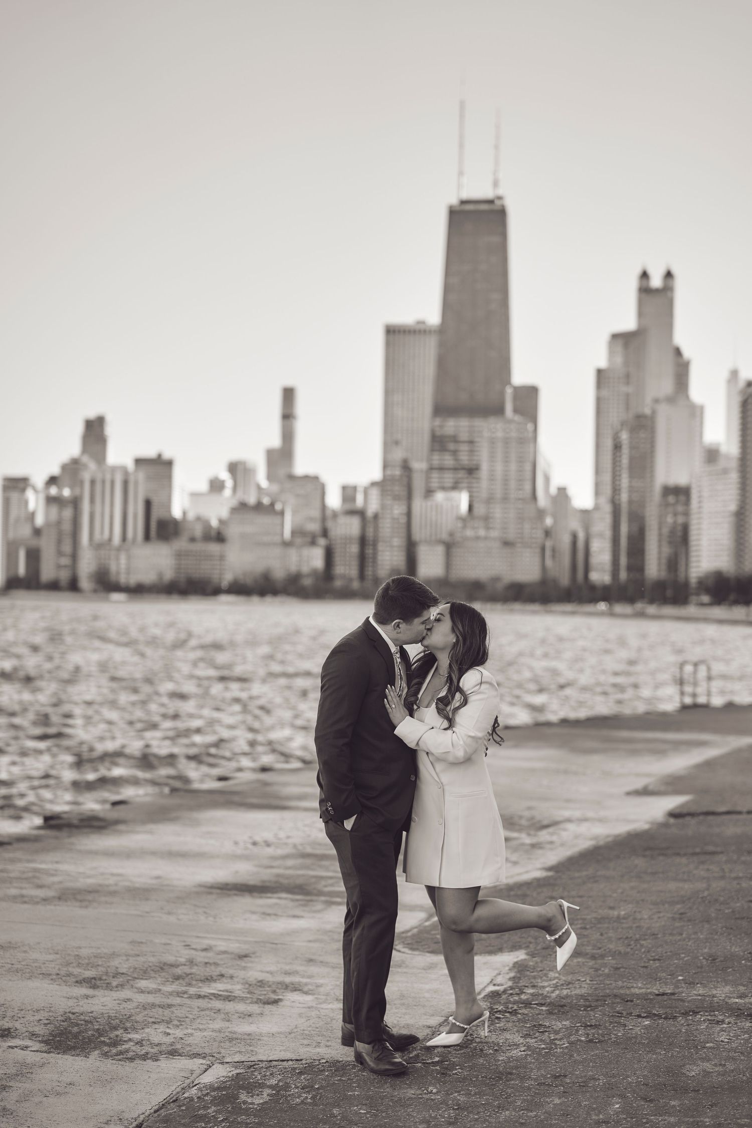 A couple shares a romantic moment on the Chicago waterfront with the iconic skyline and John Hancock building in the background.