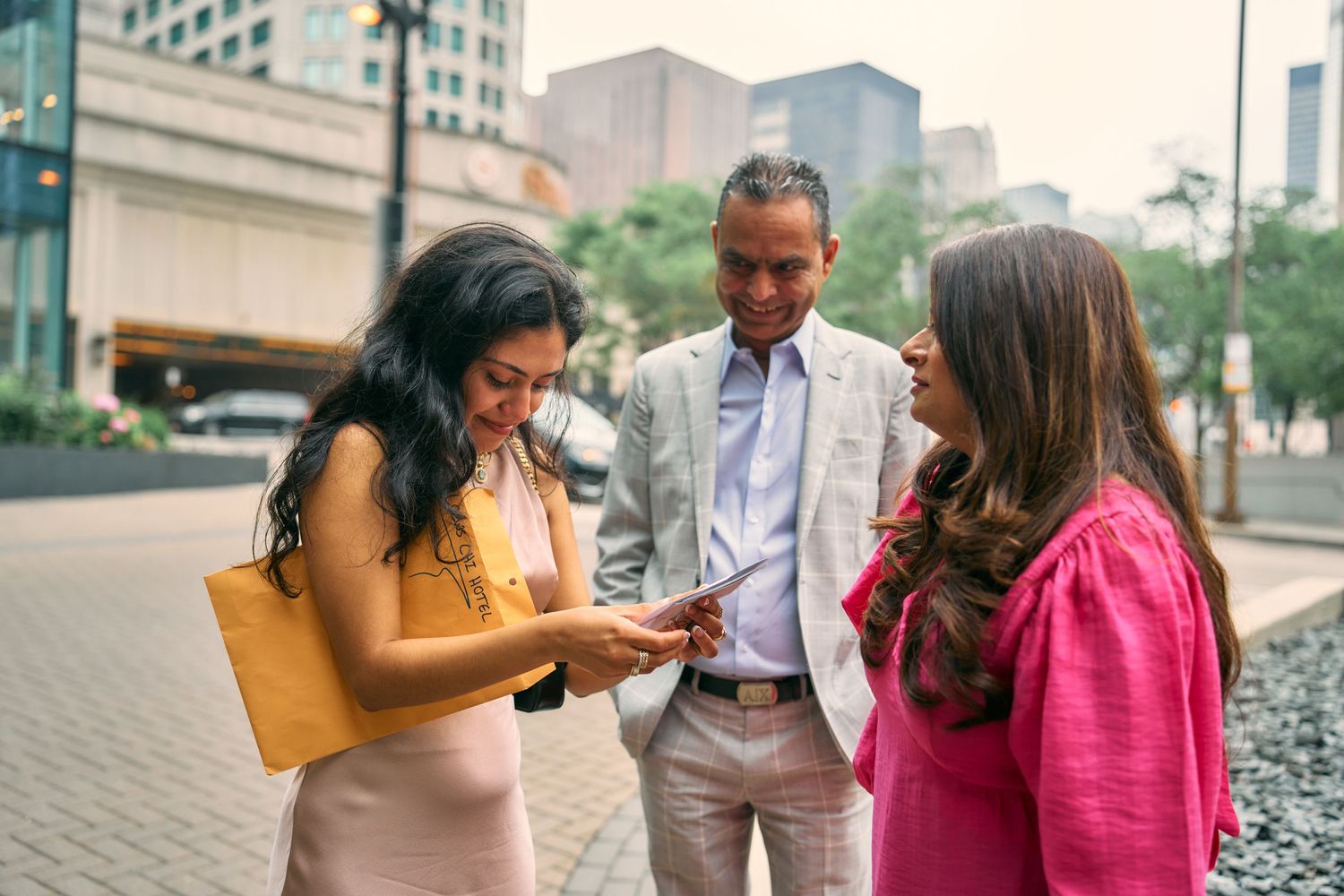 Three coworkers gathered on a city sidewalk look at a mobile phone together during their workday break.