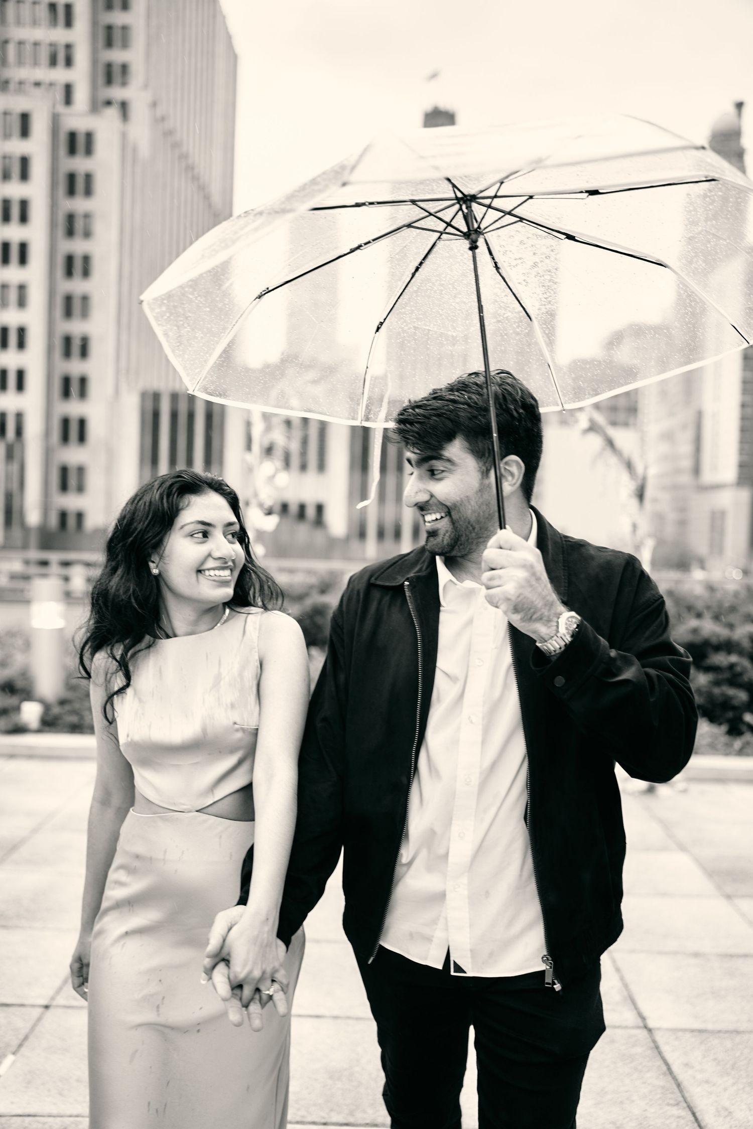 A couple shares a clear umbrella while walking in the city on an overcast day.